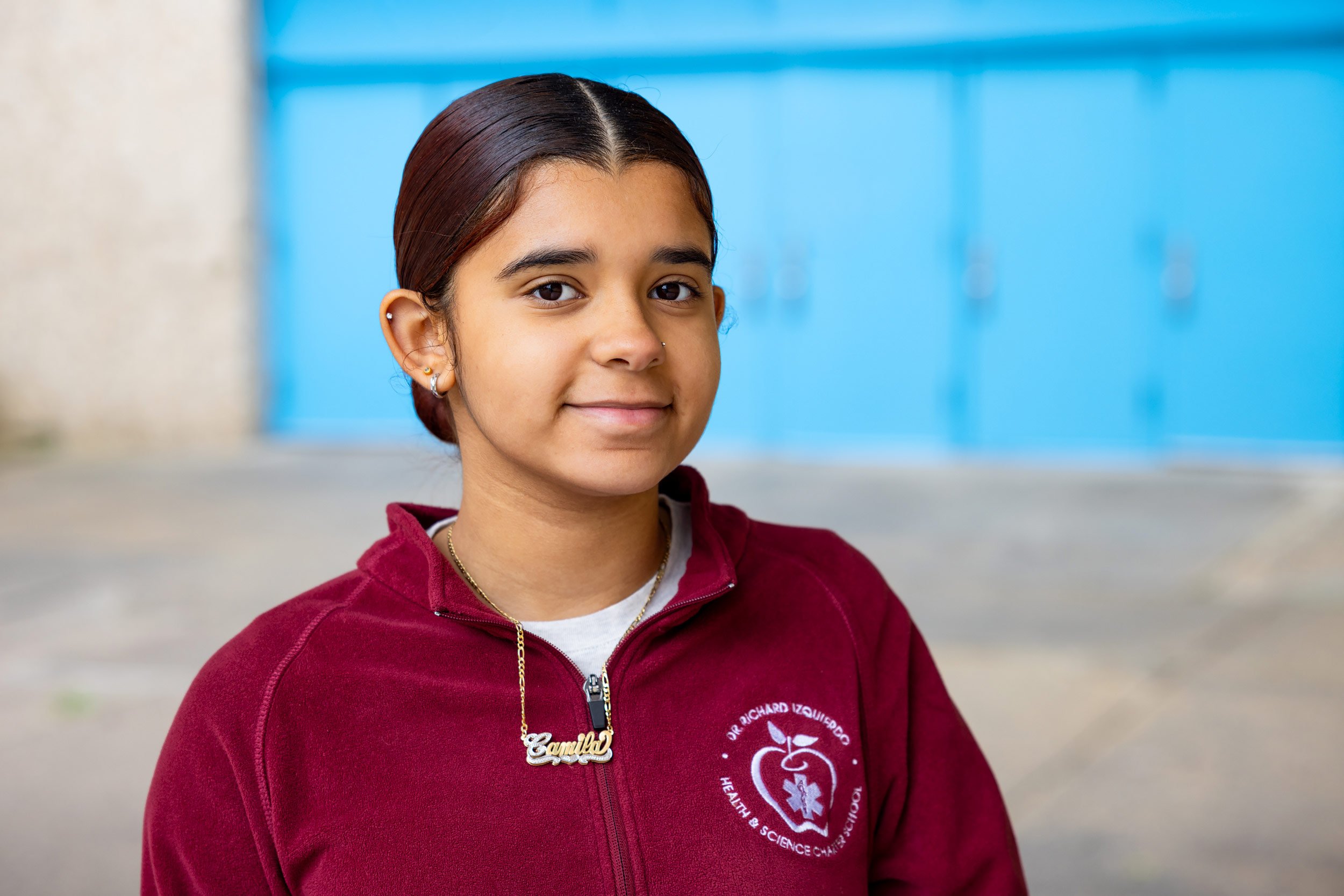 Close-up portrait of young student in red uniform against soft background outside.