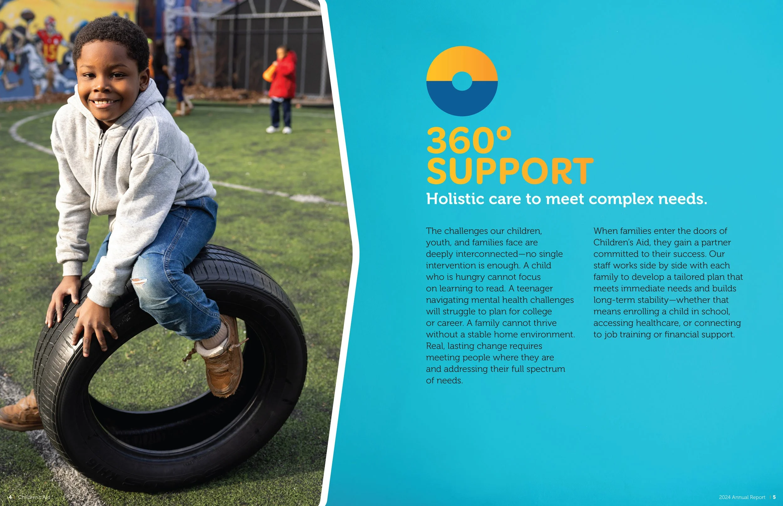 Young boy playing with a car tire in a school yard, smiling at the camera