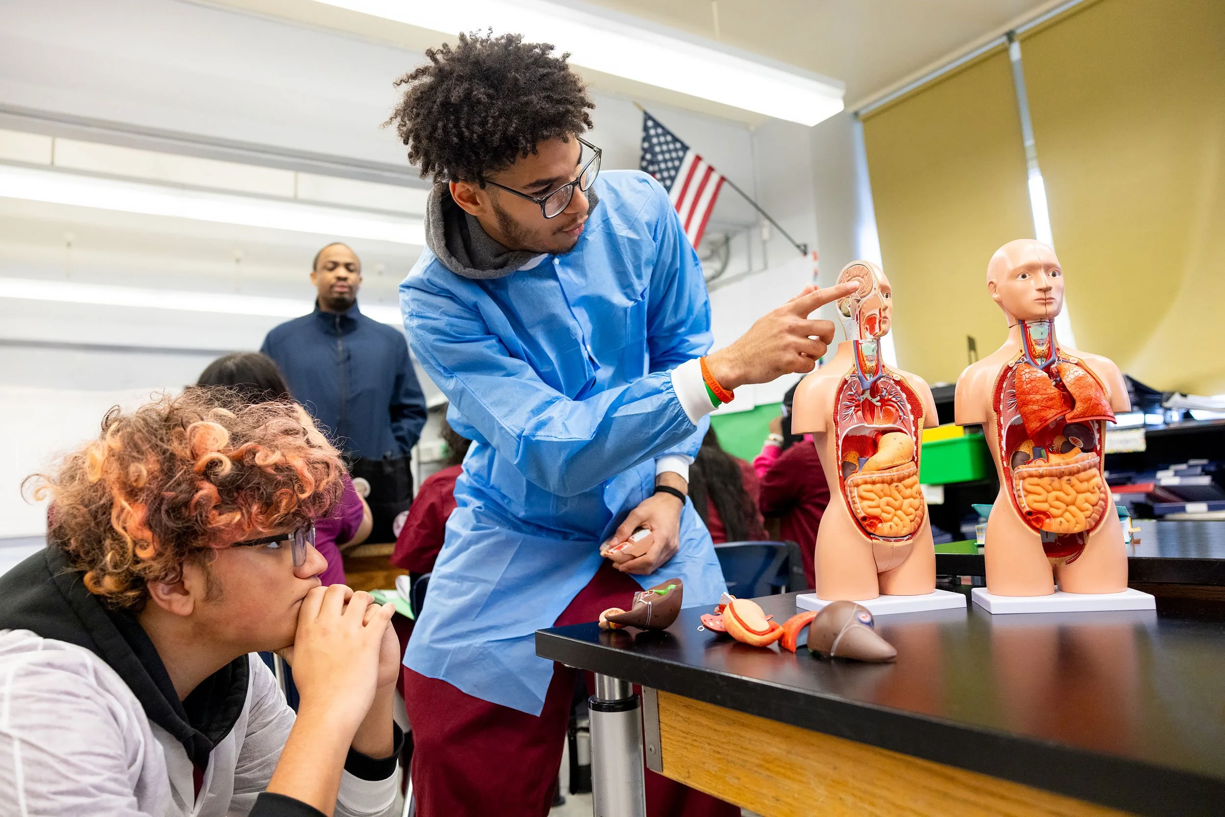 Two students wearing lab coats in a classroom examining human anatomy models