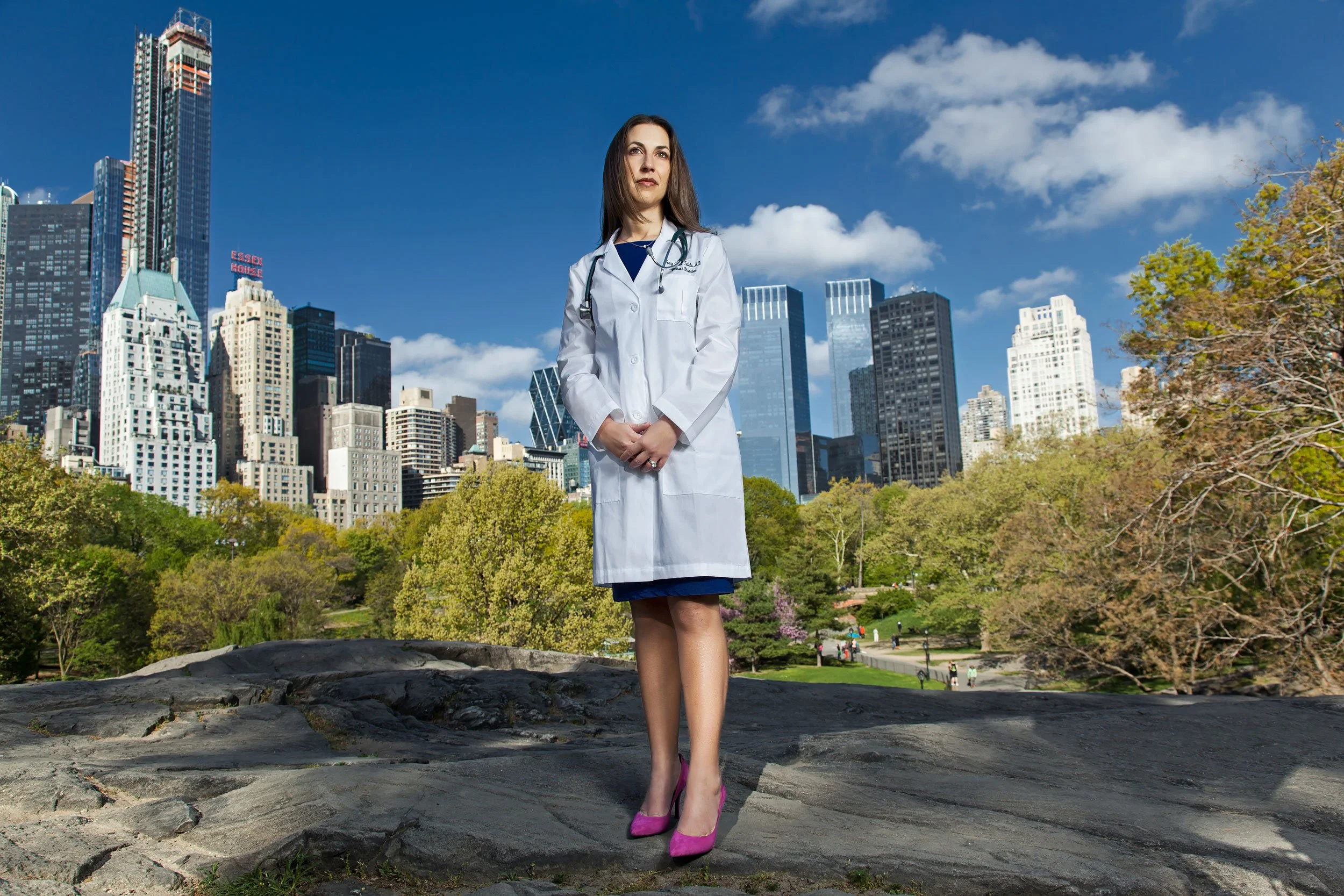 Female doctor standing on a rock in Central Park with city views wearing a white coat.