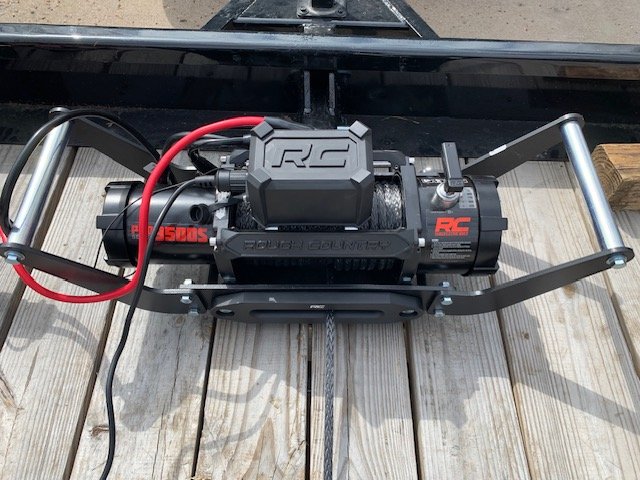 A Rough Country electric winch with cables mounted on a vehicle bumper.