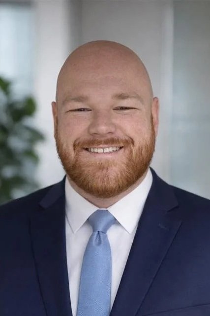 Person in a suit smiling indoors with a brick wall background.