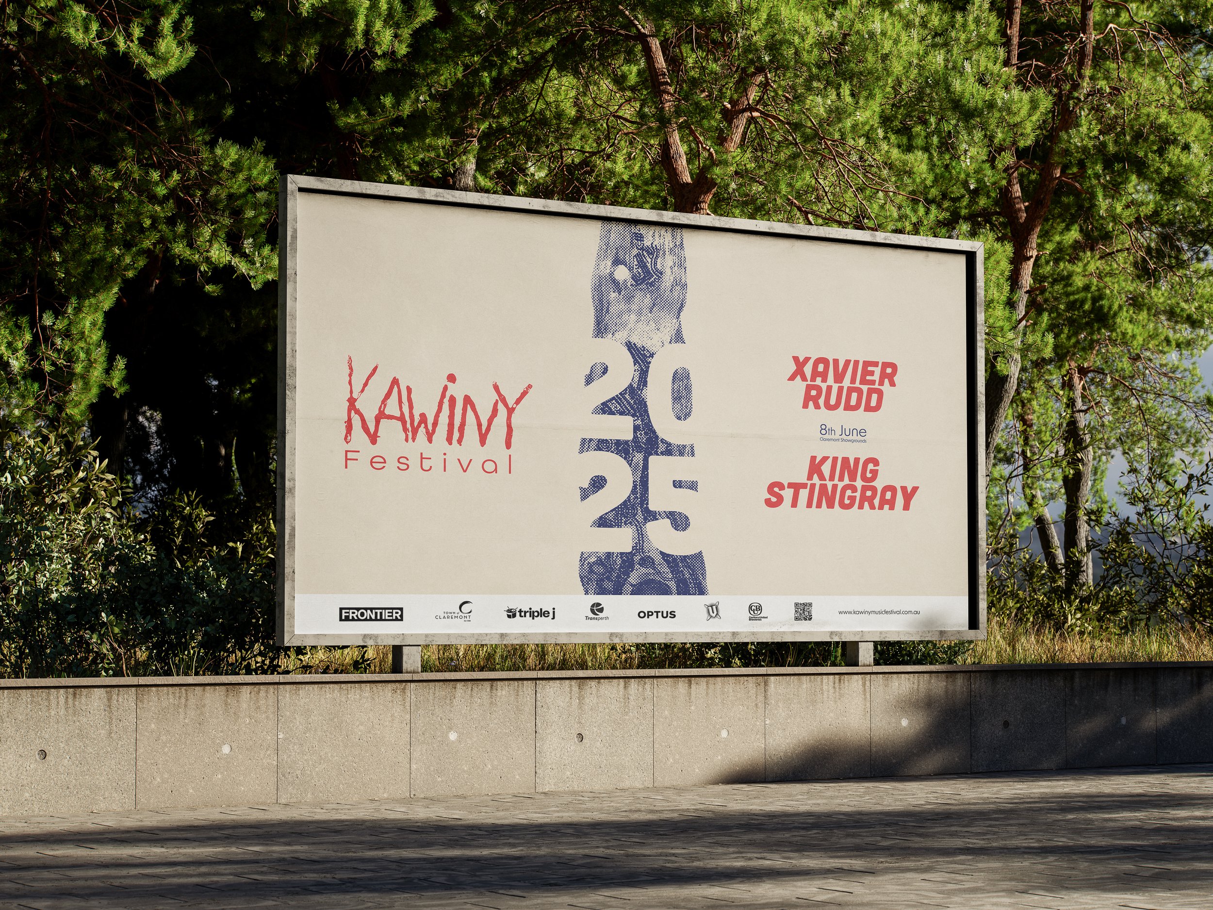 A large outdoor festival banner displaying the name 'Kawiny Festival' with a list of performers including Xavier Rudd and King Stingray, against a background of green trees.
