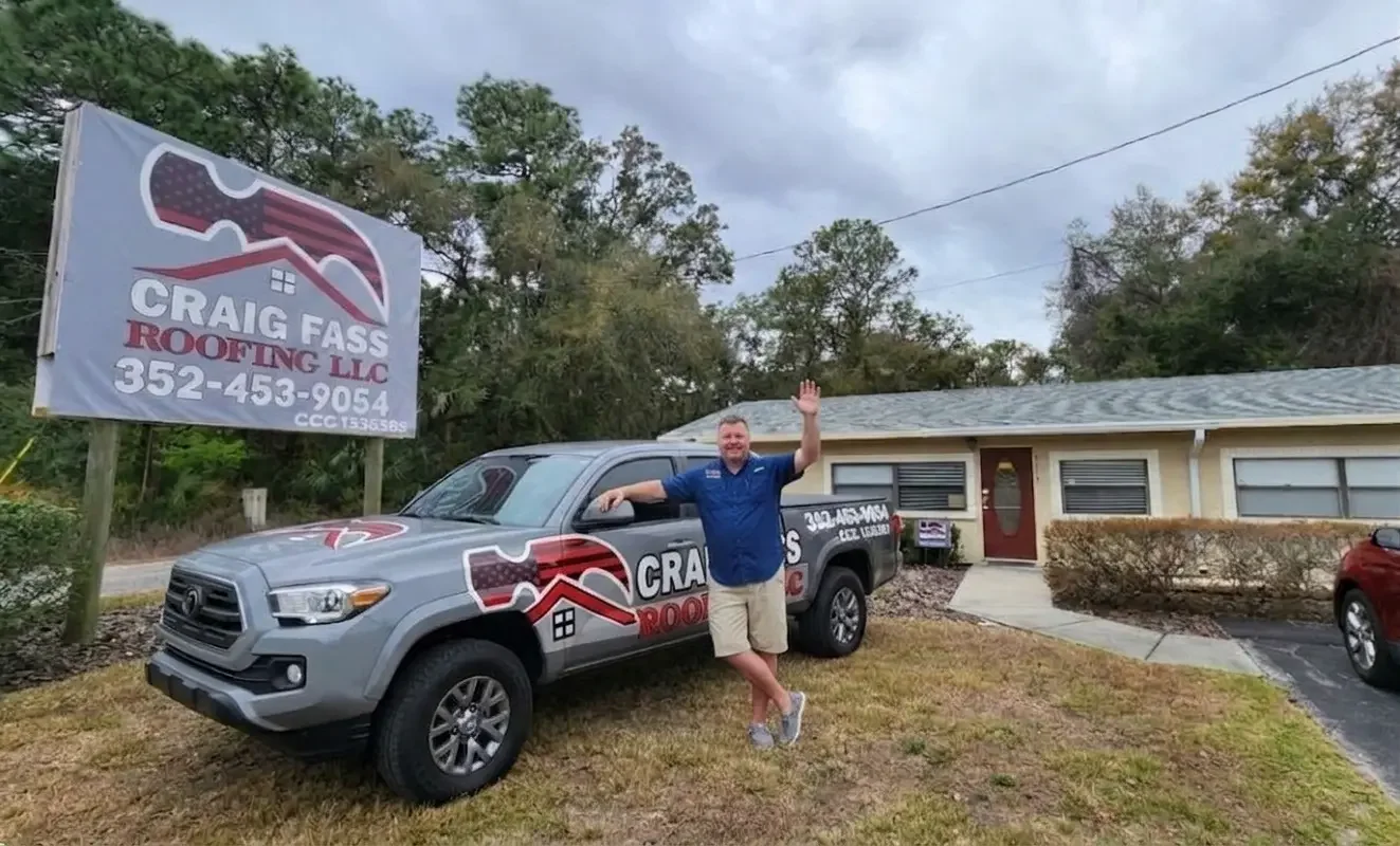 Local roofing contractor Craig Fass waving next to a Craig Fass Roofing company truck and yard sign at the main office, right across from Sugarmill Woods in Citrus County.
