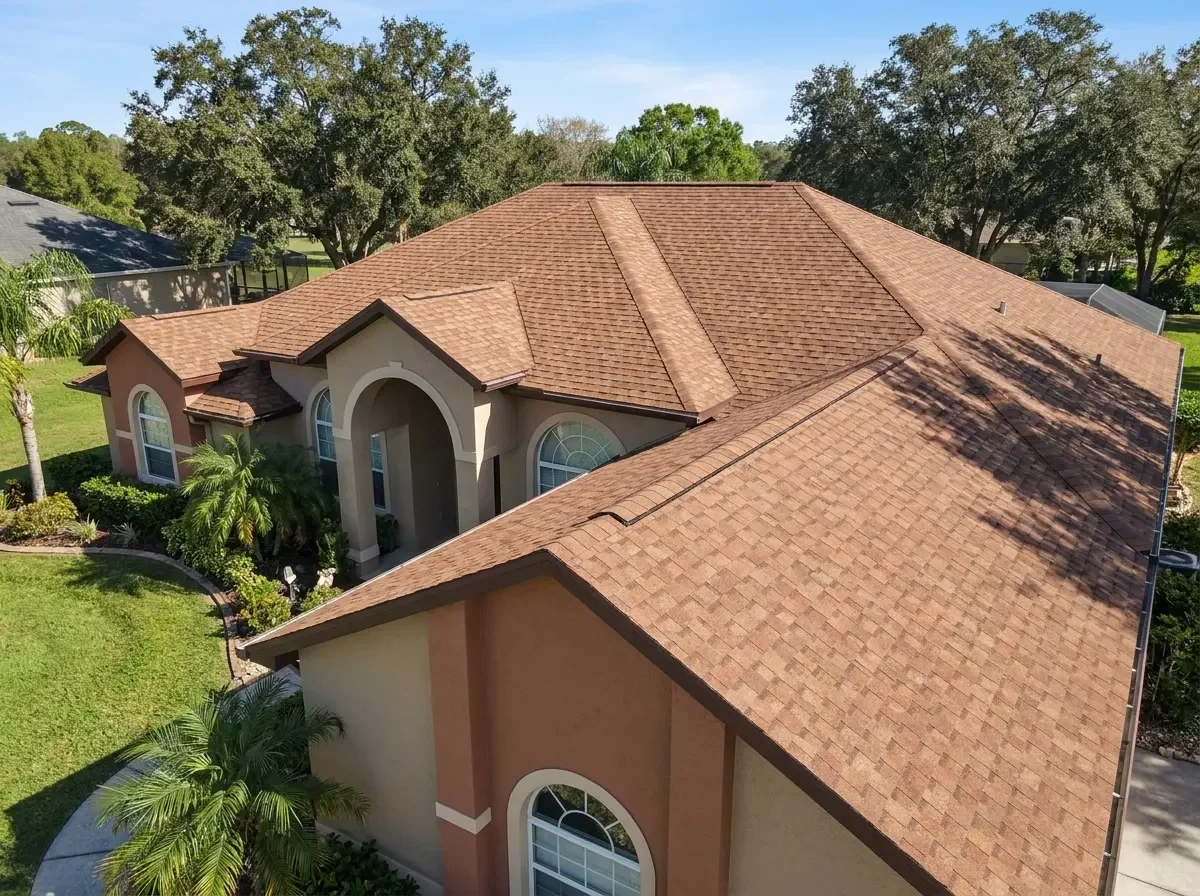 A pristine new asphalt shingle roof on an earth-tone suburban estate in Inverness, FL, completed by Craig Fass Roofing and surrounded by manicured lawns and palm trees.