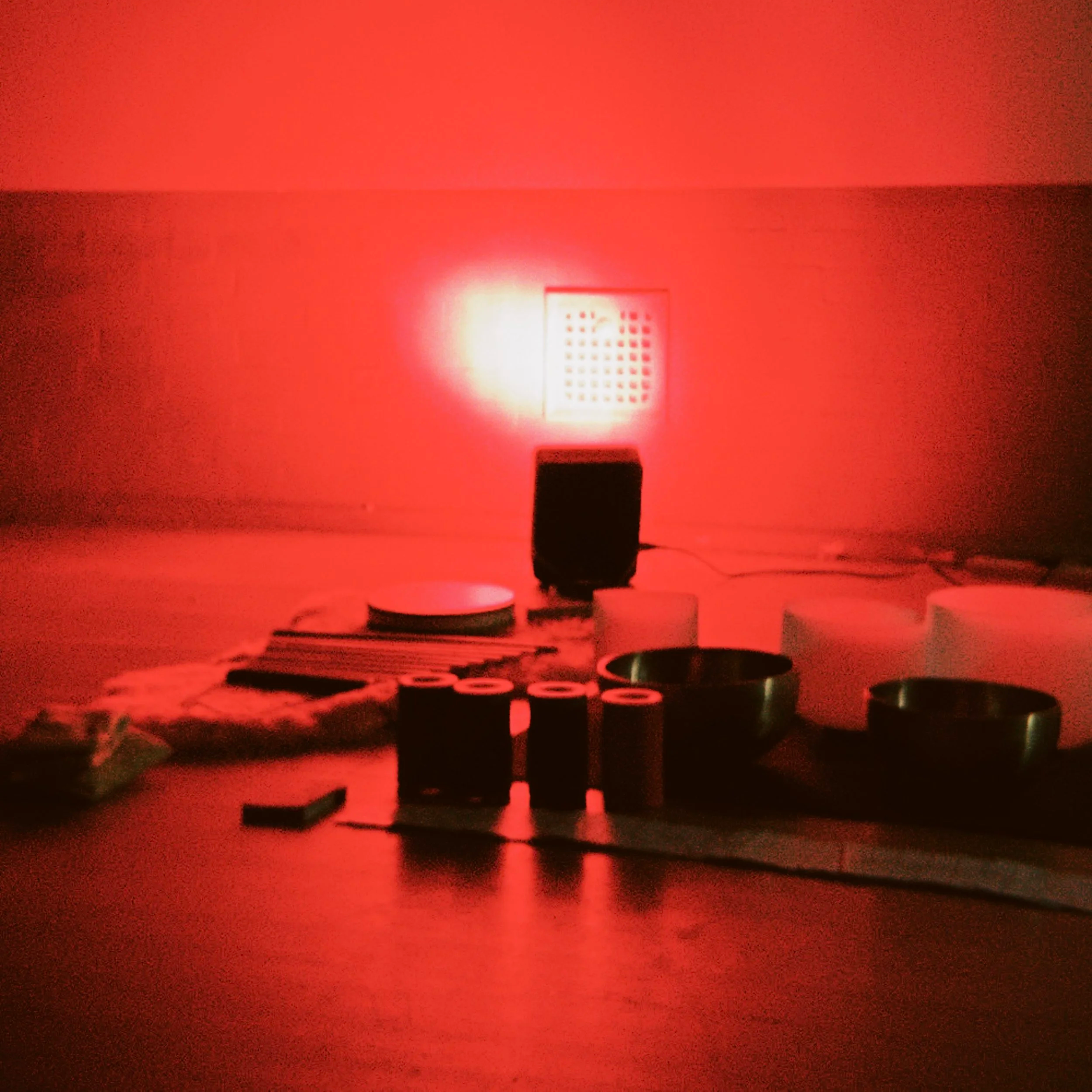 A red room with a vent or grille on the wall, a black object with multiple projection buttons or controls, and a smaller white object in the foreground.