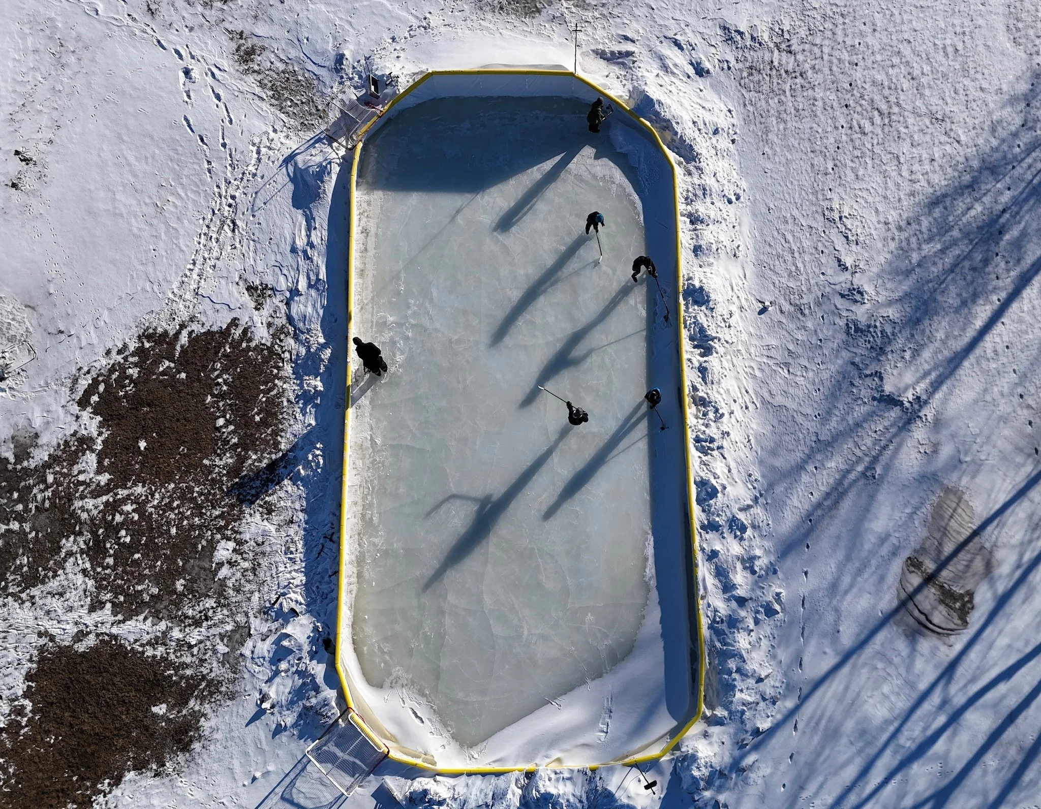 overhead image of backyard ice rink with kids skating and adult shoveling