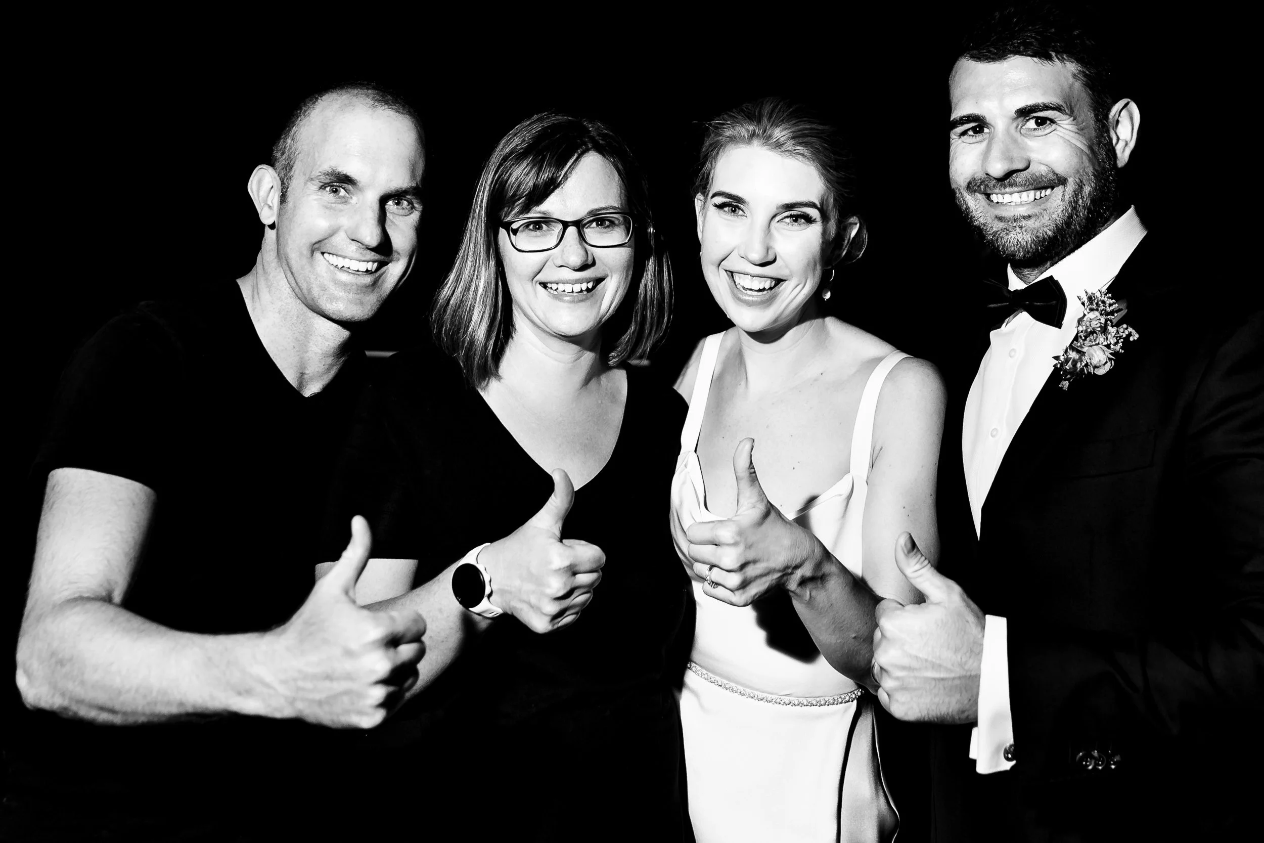 Lynn & Justin - Hunter Valley & Port Stephens wedding photographers, smiling and giving a thumbs-up with one of their wedding couples against a black background, in black and white.