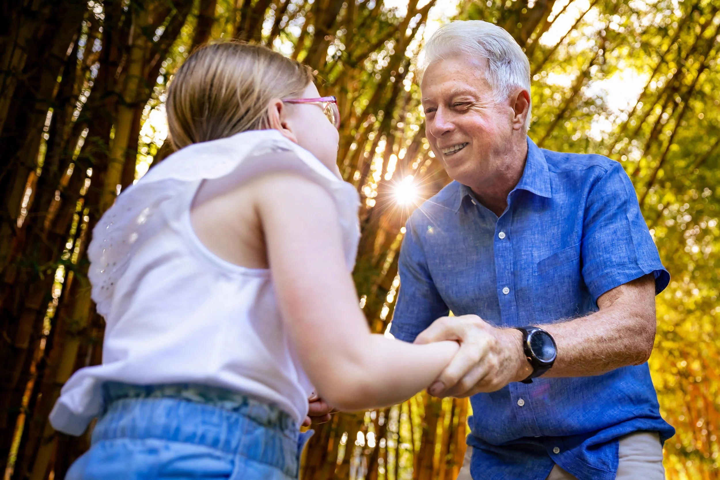 A young girl and an elderly man in Singleton, NSW, shaking hands outdoors in a park with trees and sunlight in the background.