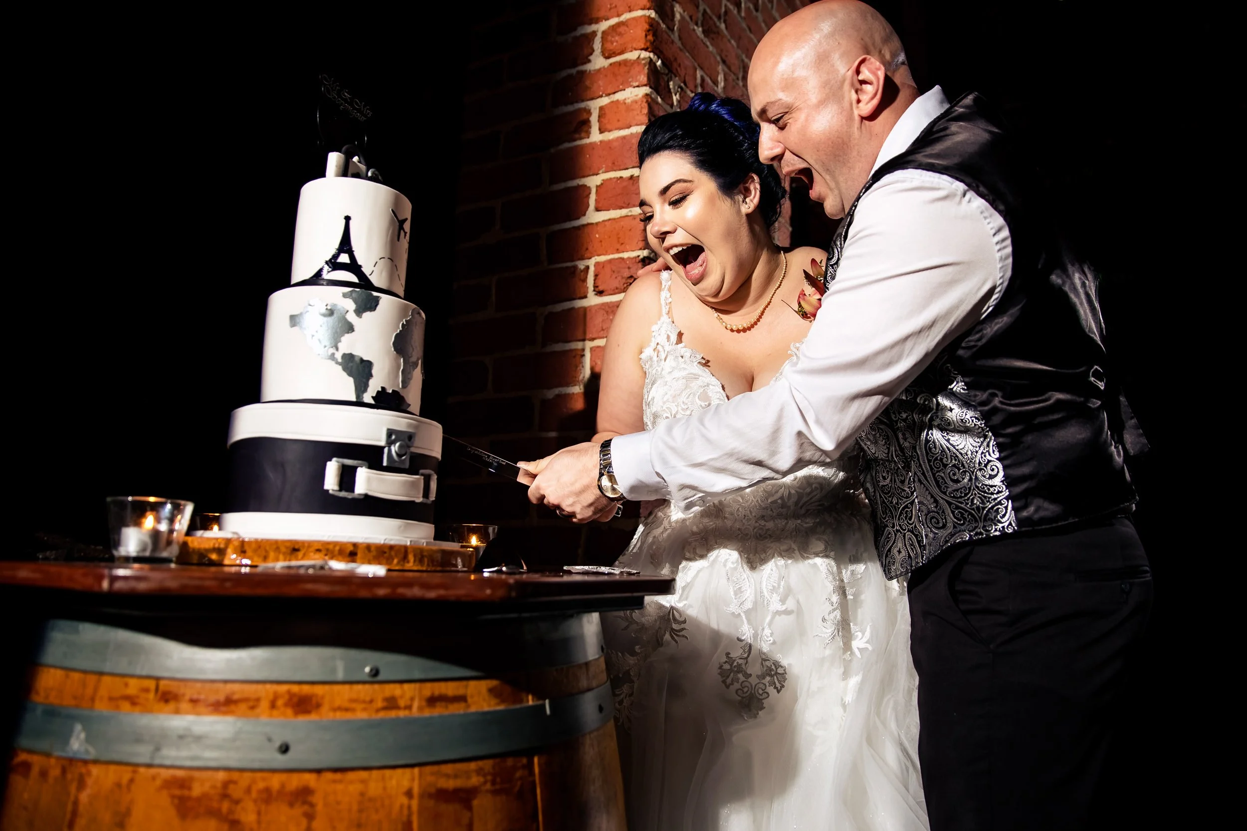 A bride and groom celebrate with a cake cutting at their wedding reception at Sirromet Winery, Brisbane. The cake has a world map and Eiffel Tower decoration. Captured by Port Stephens wedding photographers, Lynn & Justin.