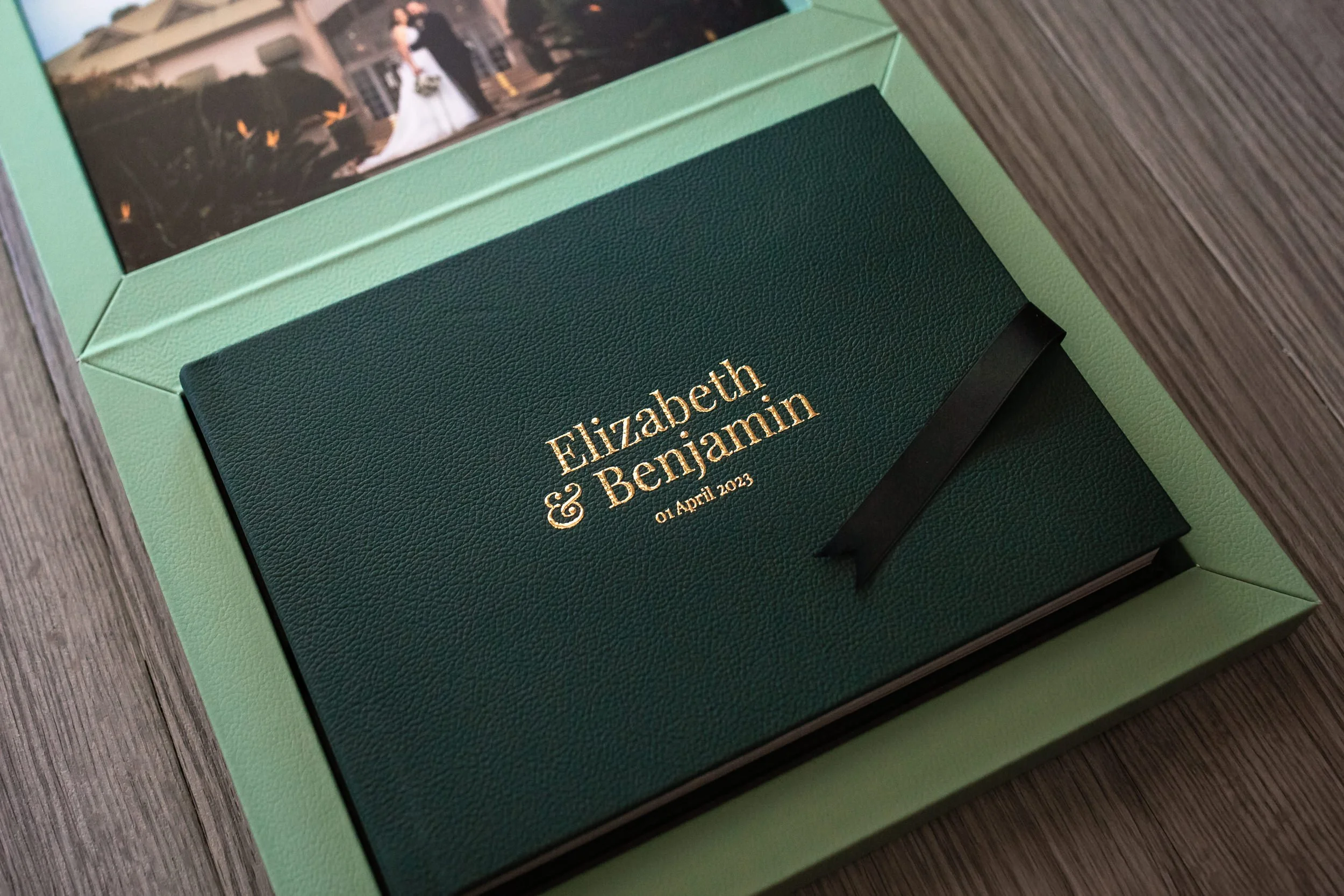 A green textured card box with gold embossed text displaying the names, inside a larger light green box on a wooden surface. This is the album given to wedding couples by Lynn & Justin, Hunter Valley & Port Stephens wedding photographers.