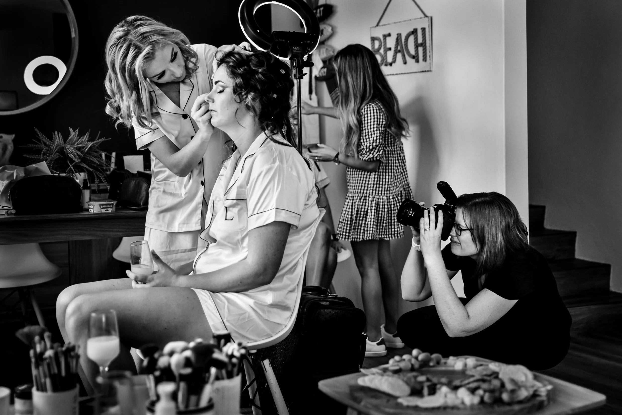 A bride getting her makeup done by a makeup artist while another Lynn, the wedding photographer, takes photos in an apartment in Port Stephens, decorated in a beach theme.