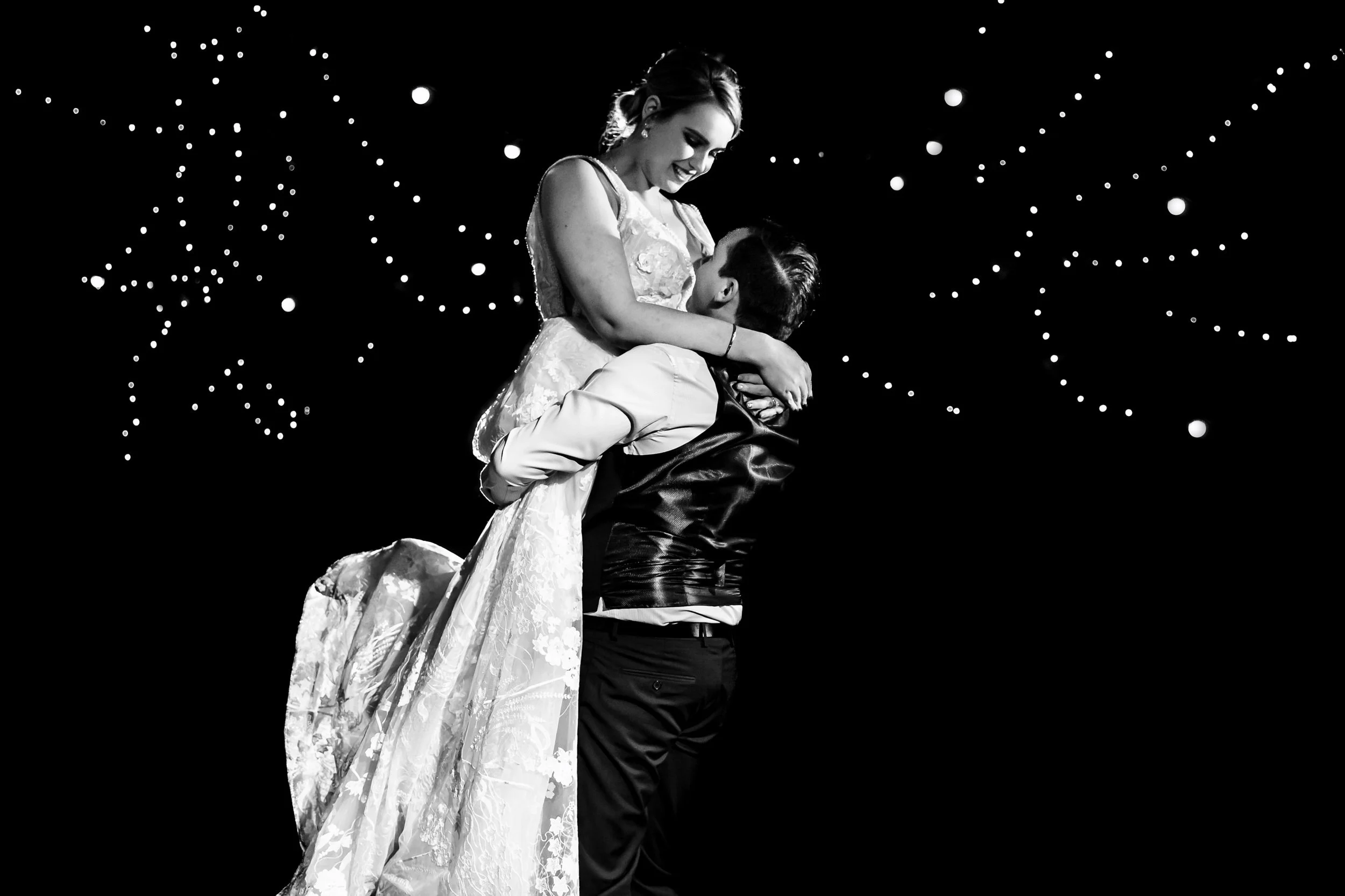 A Port Stephens bride and groom embrace during their first dance at their wedding reception, smiling, with a starry background in black and white.