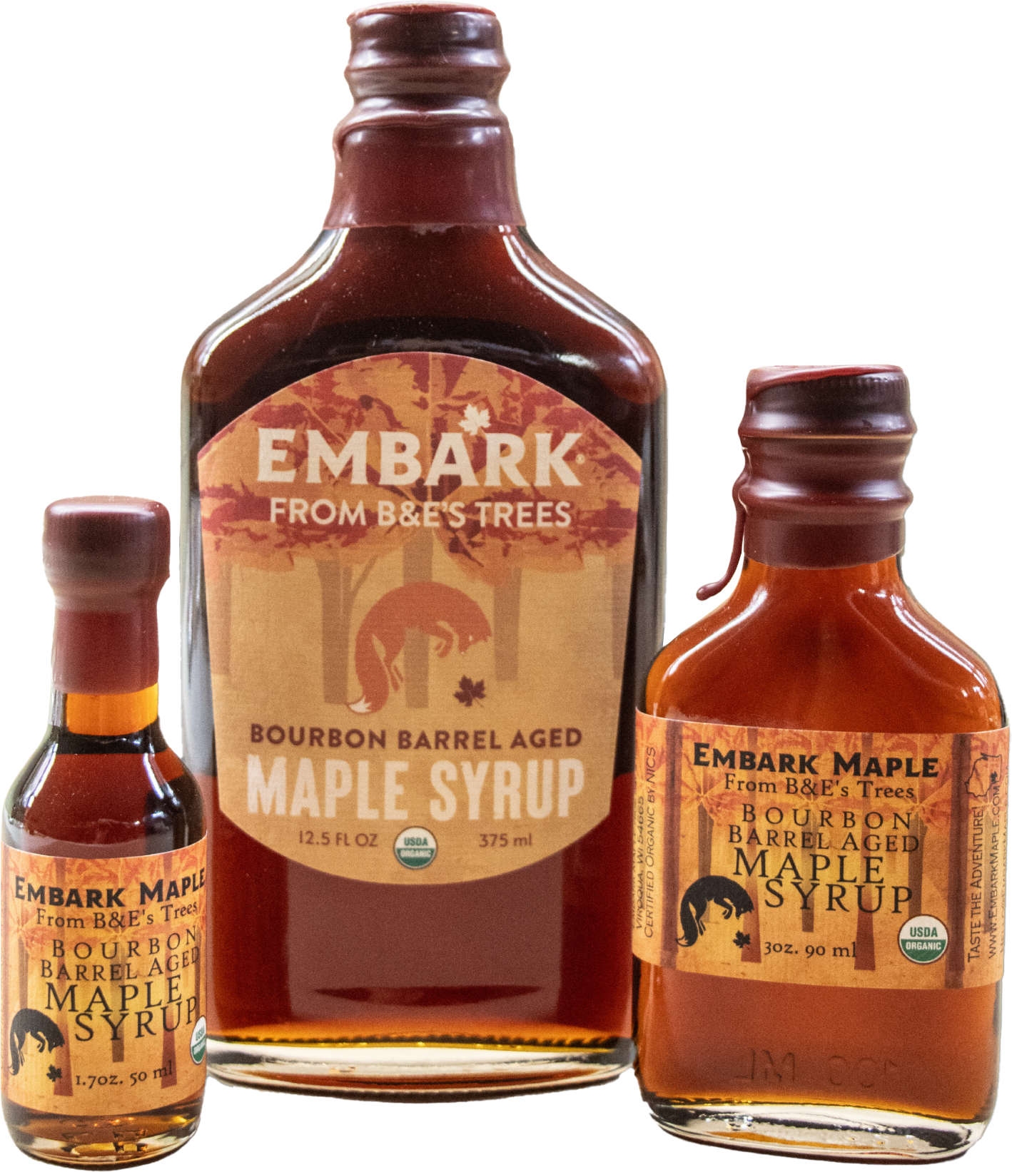 Three bottles of Mark's Maple Syrup from B&E's Trees, varying in size, with labels indicating bourbon barrel aged maple syrup and maple syrup, featuring a tree and horse design, and USDA organic certification.