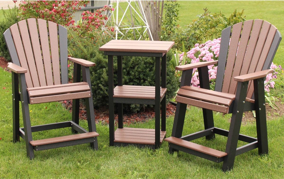 Outdoor patio setting with two Adirondack chairs and a small table on grass, surrounded by bushes and pink flowers.
