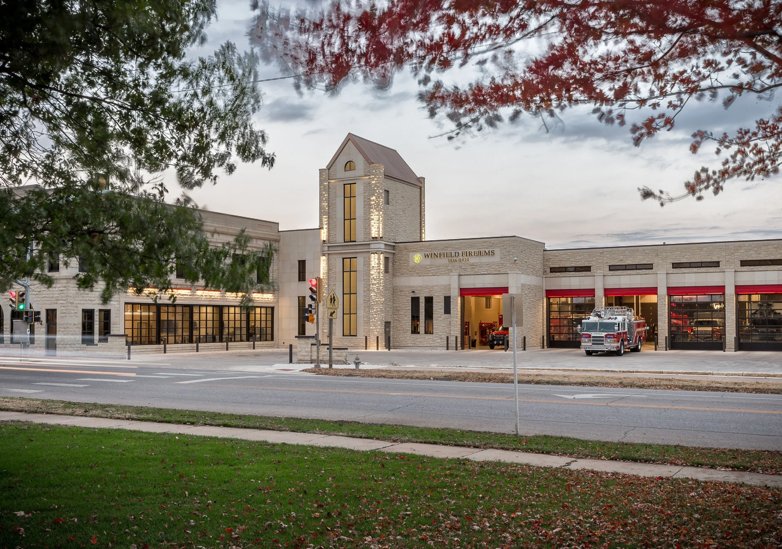 Winfield Fire Station with fire trucks parked inside and outside, surrounded by trees and a street with traffic signals.