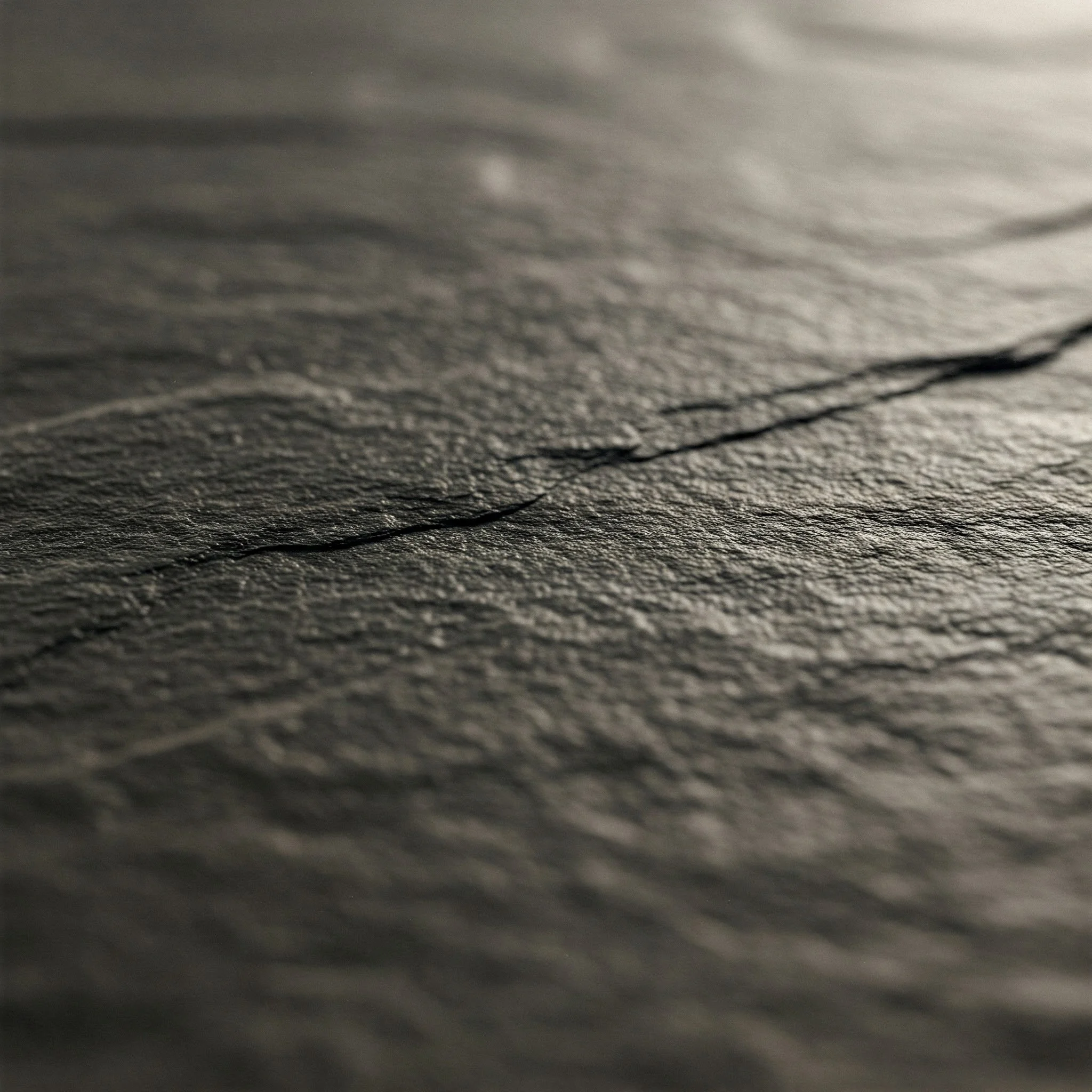 Close-up of textured dark gray paper with visible fibers and a prominent crack running across the surface.