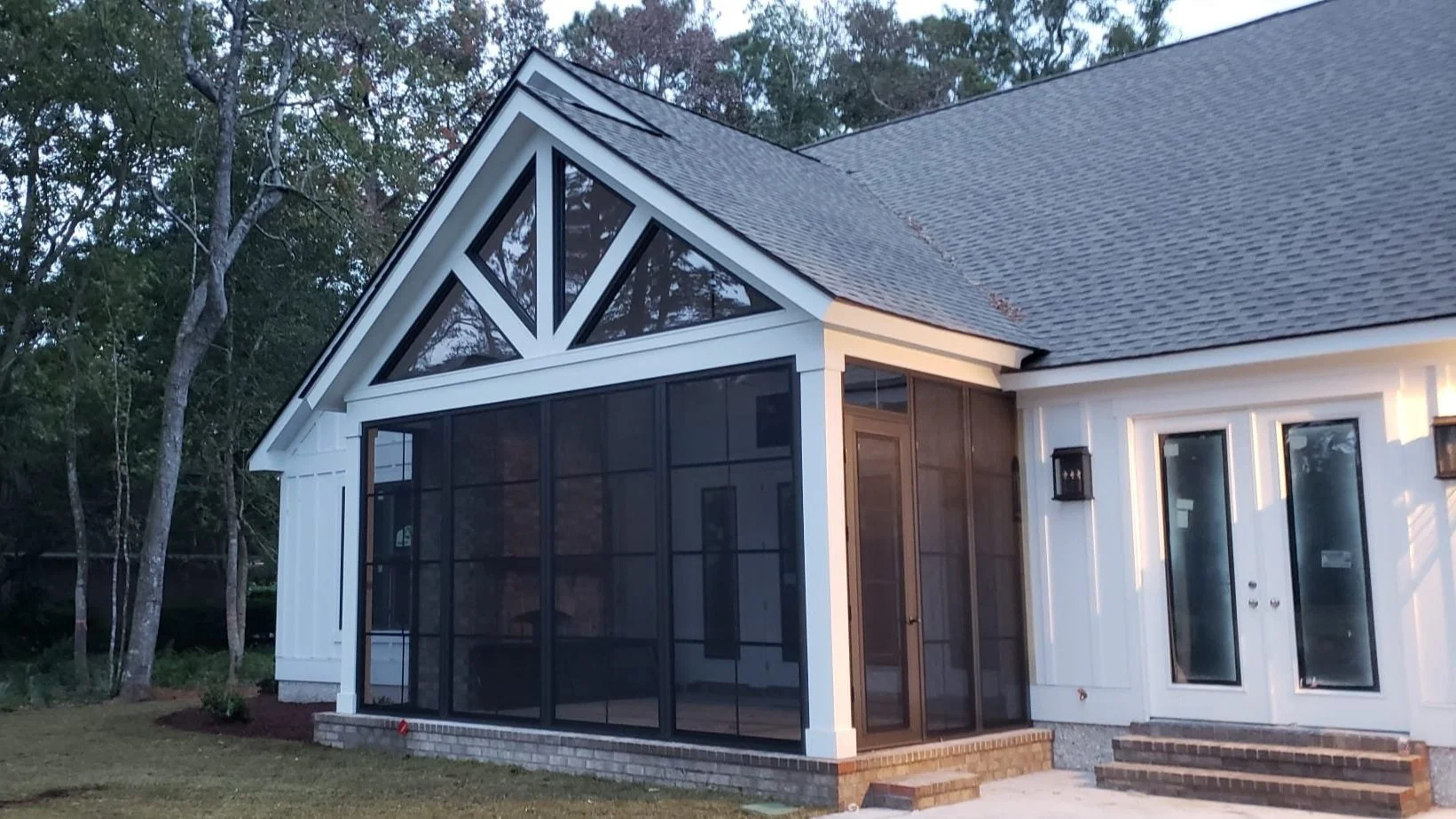 A modern house with a screened porch, white siding, multiple windows, and a gabled roof surrounded by trees.