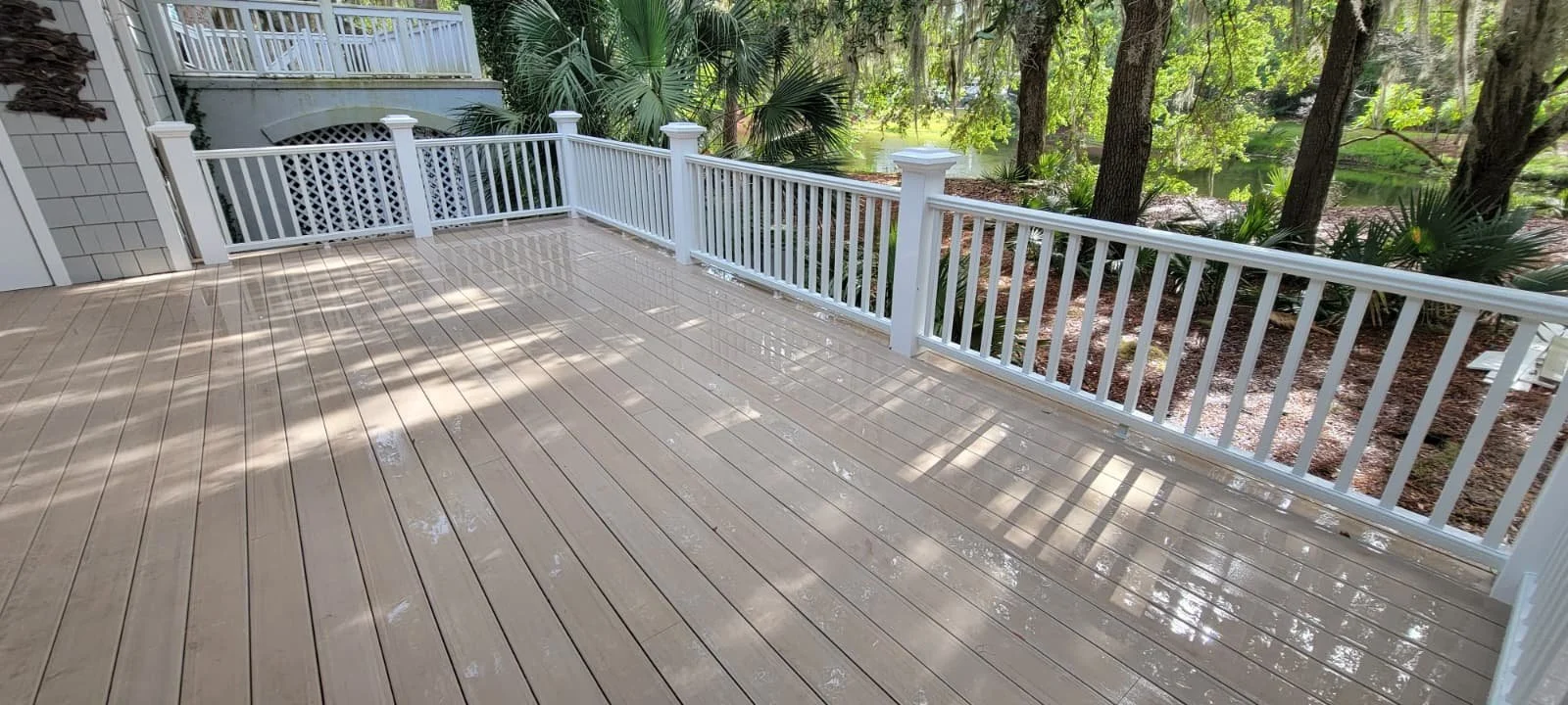 A clean, wet wooden deck with white railing overlooking a lush, green, wooded backyard.