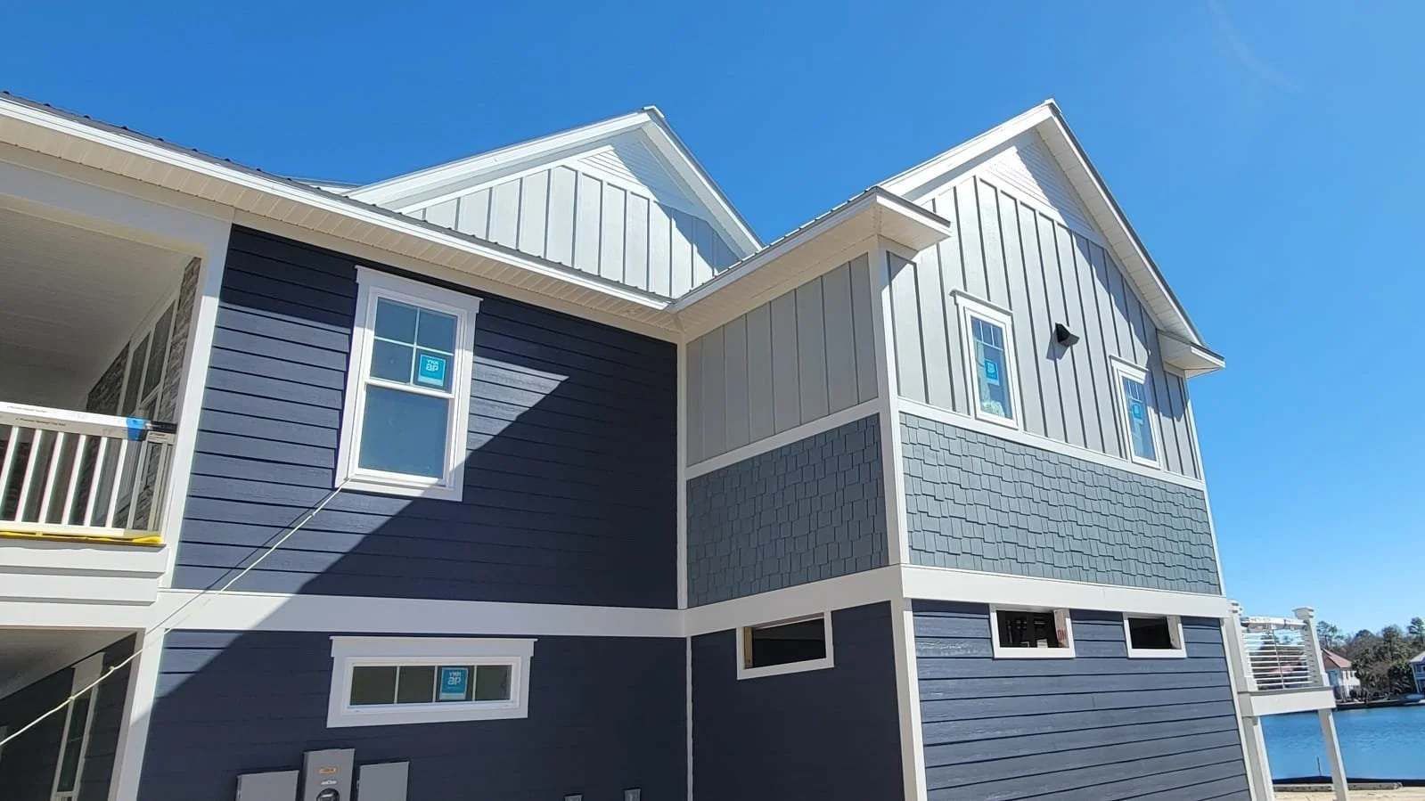 Modern two-story house with blue and gray siding, multiple small windows, and a waterfront view.