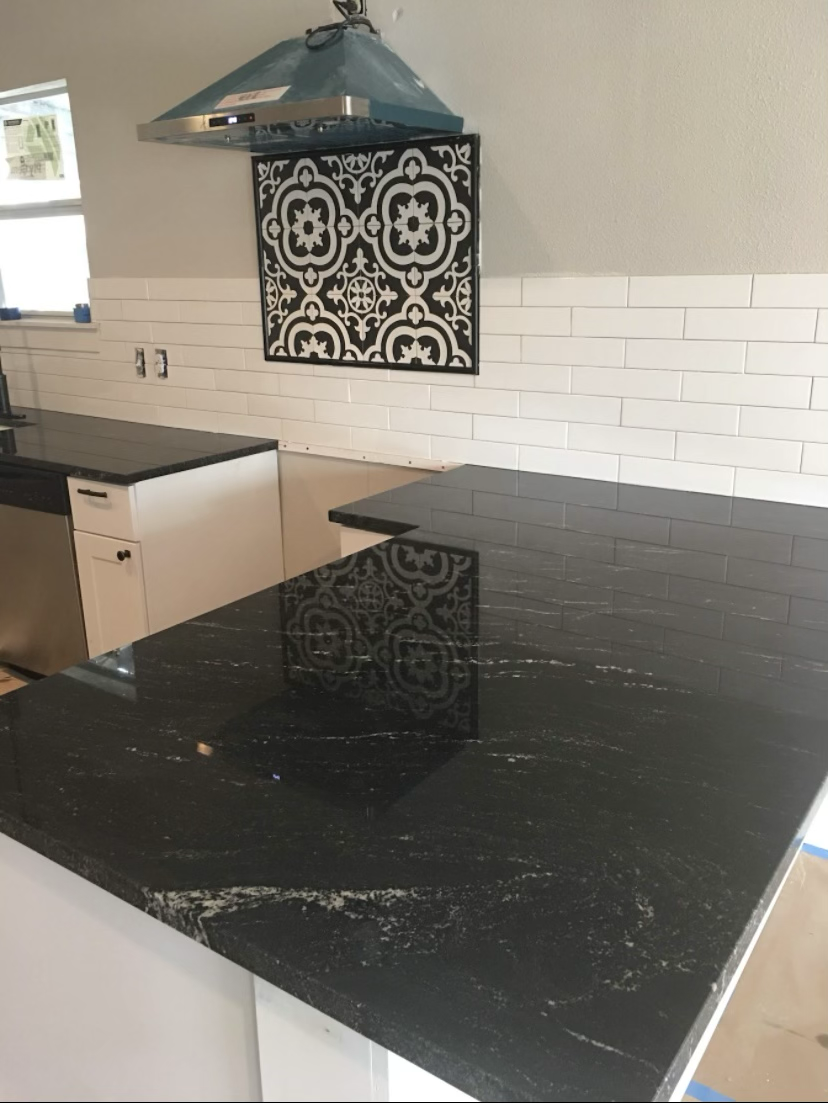 Modern kitchen with black granite countertops, white subway tile backsplash, decorative black and white tile accent, and stainless steel range hood.