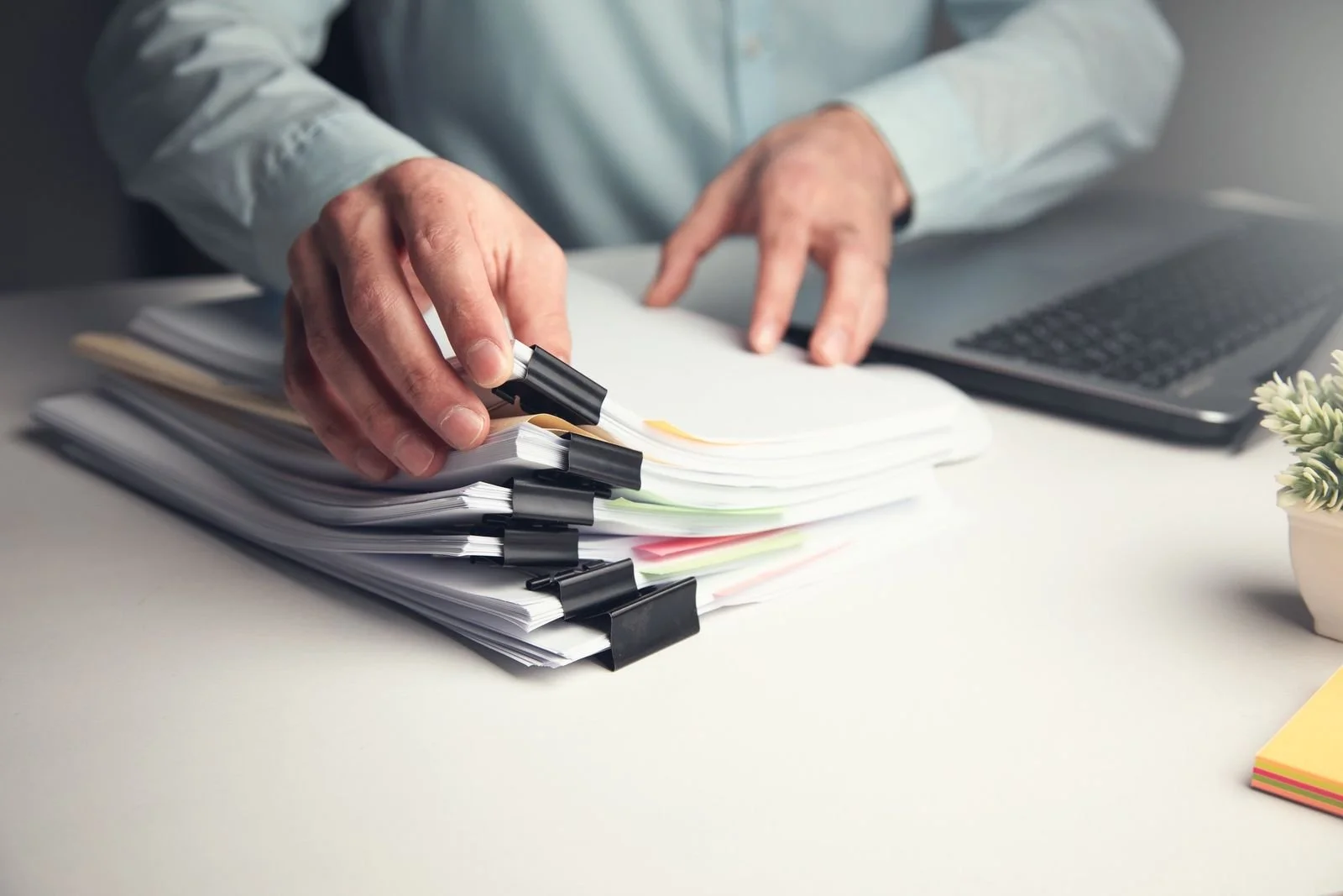 Hands reviewing a stack of trade documents beside a laptop
