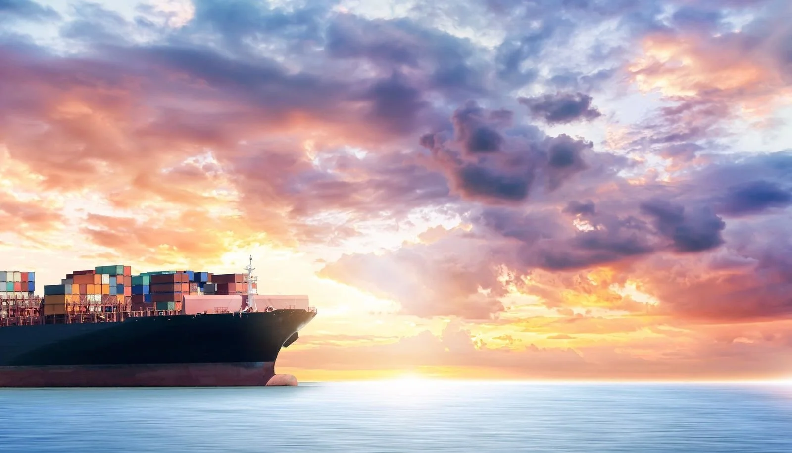 Loaded container ship at sea under a sunset sky