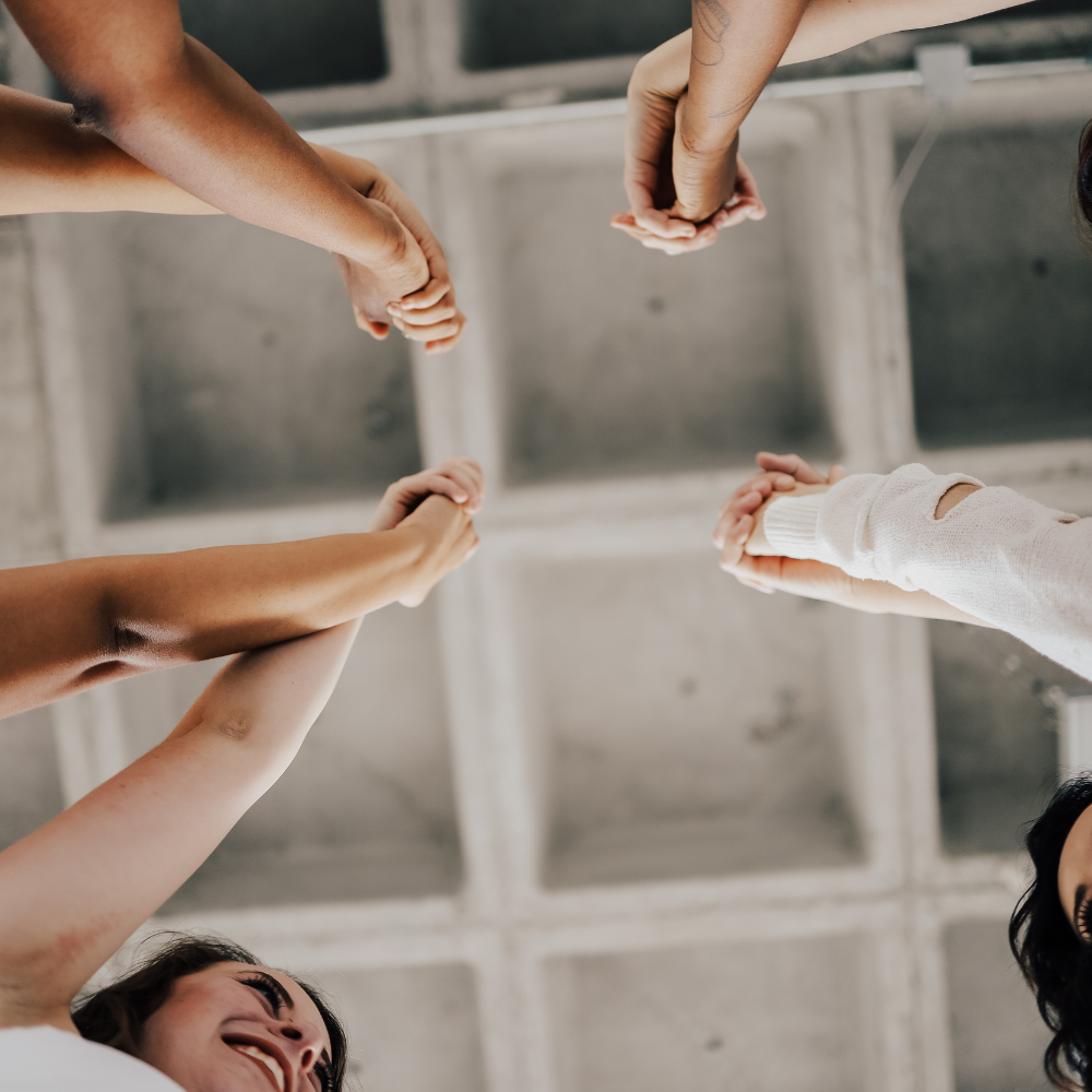 Group of diverse people holding hands in a circle, viewed from below.
