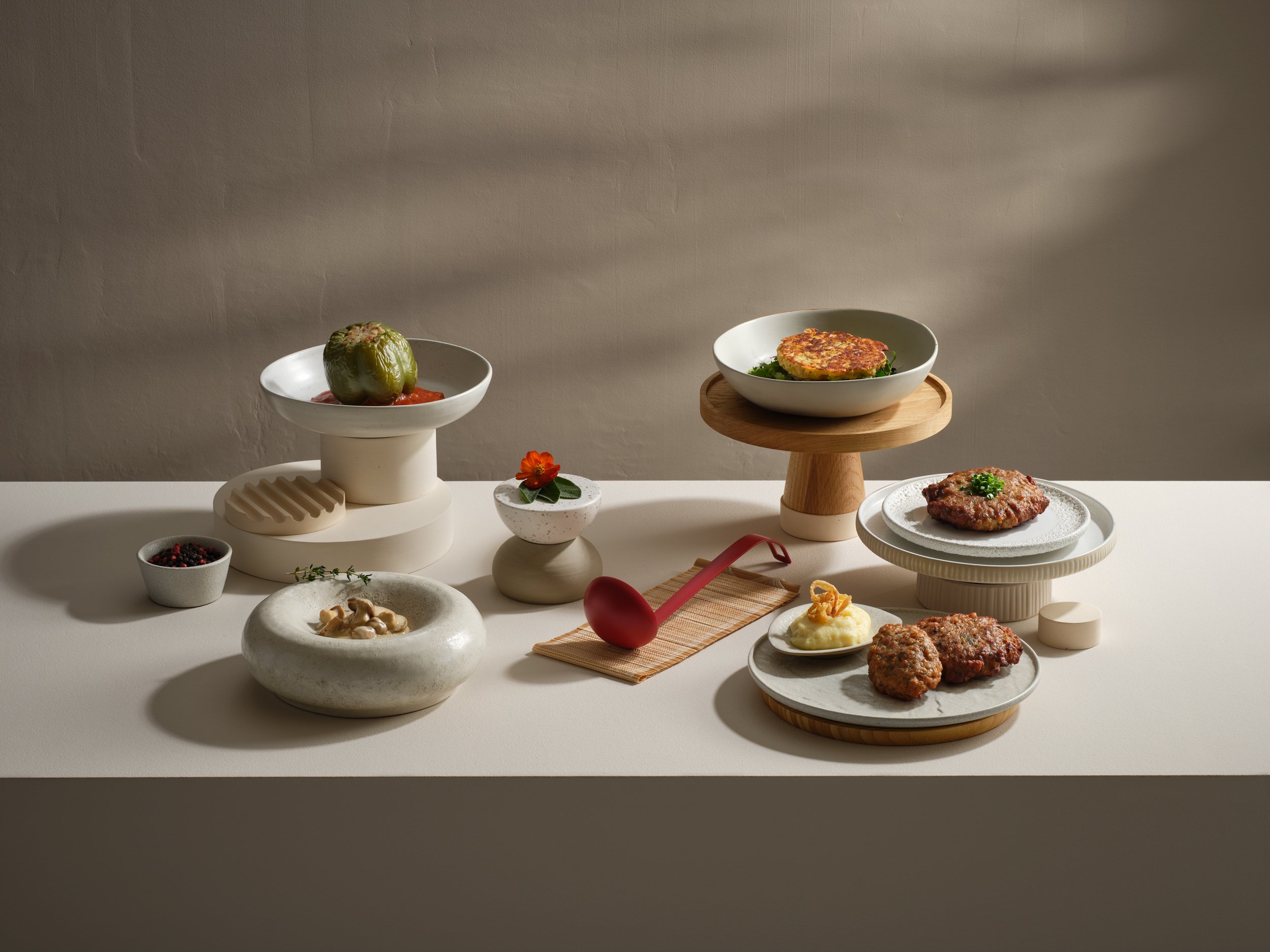 Verschiedene Fleischgerichte und Beilagen auf eleganten Tellern und Servierplatten, arrangementiert auf einem weißen Tisch mit minimalistischer Dekoration.