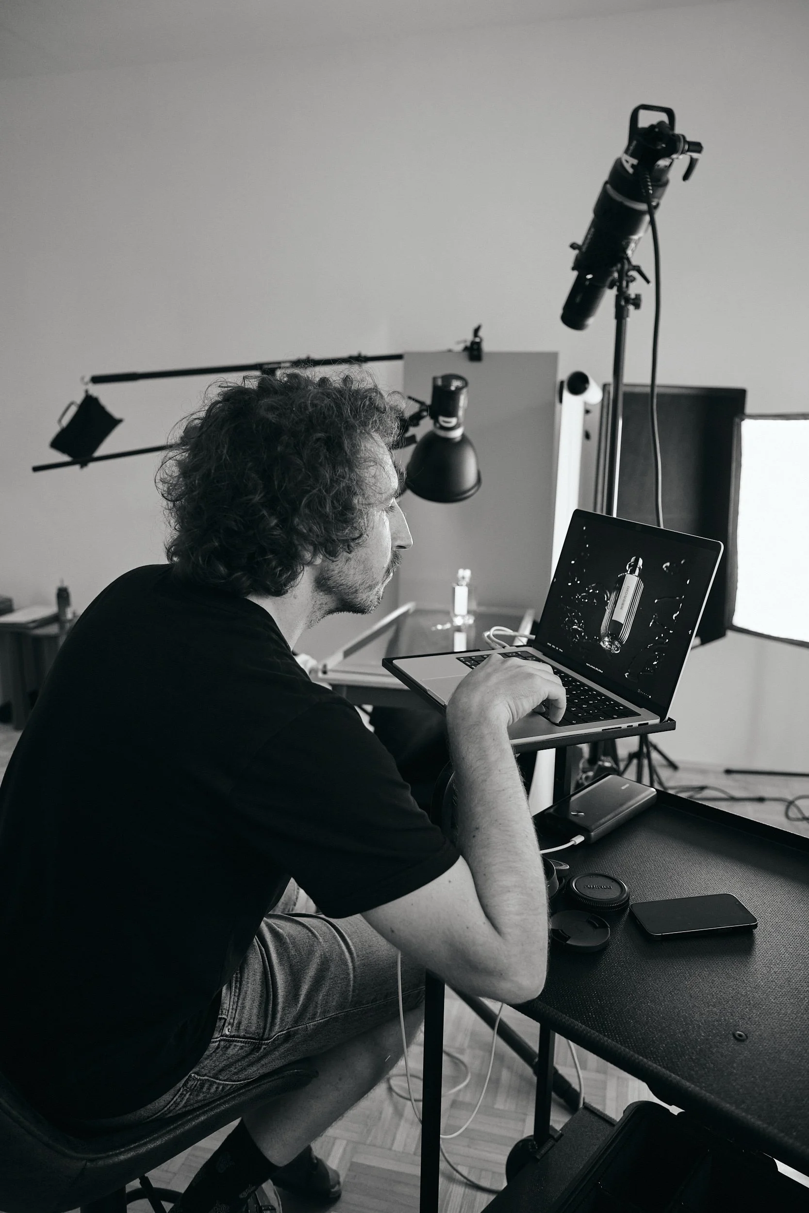 Ein Mann mit lockigem Haar arbeitet an einem Laptop in einem professionellen Studio mit Studiobeleuchtung und einem Teleskop.