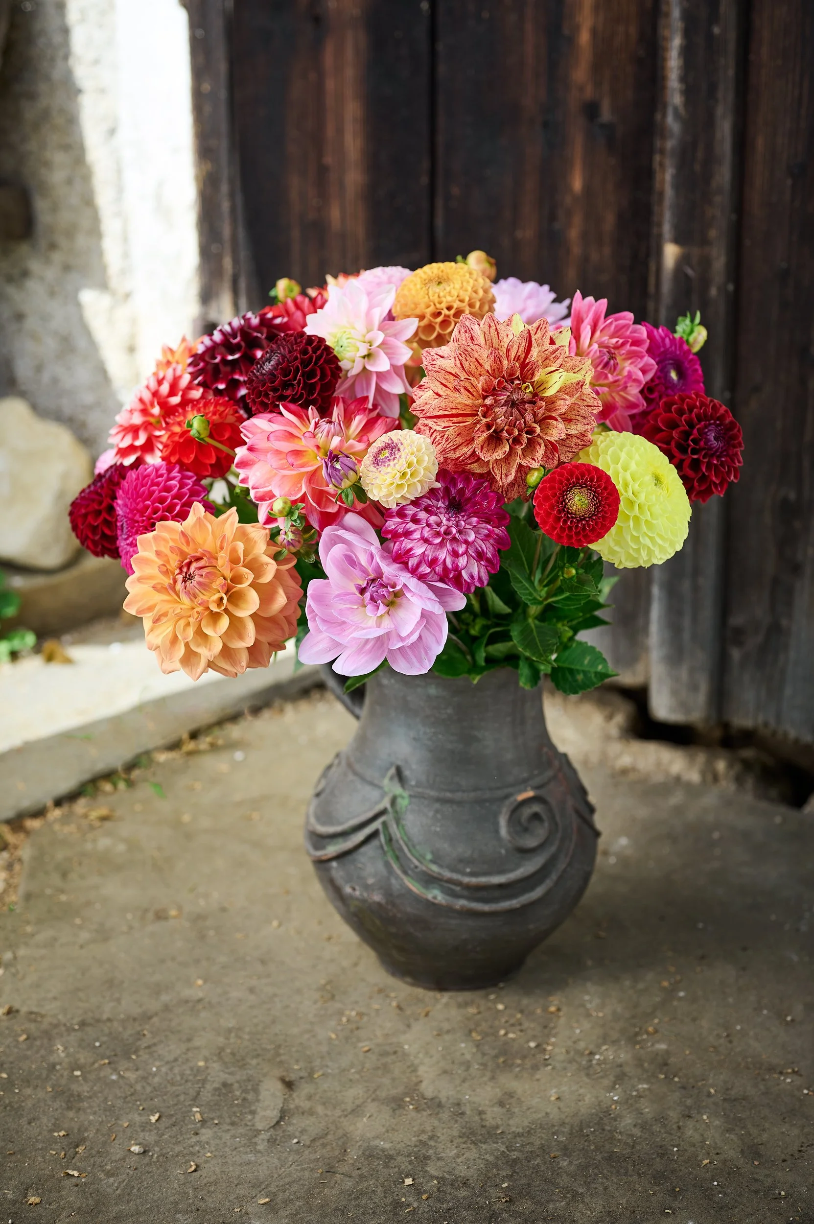 Ein Blumenstrauß mit bunten Dahlien in einer Vase auf einem Steinsockel.