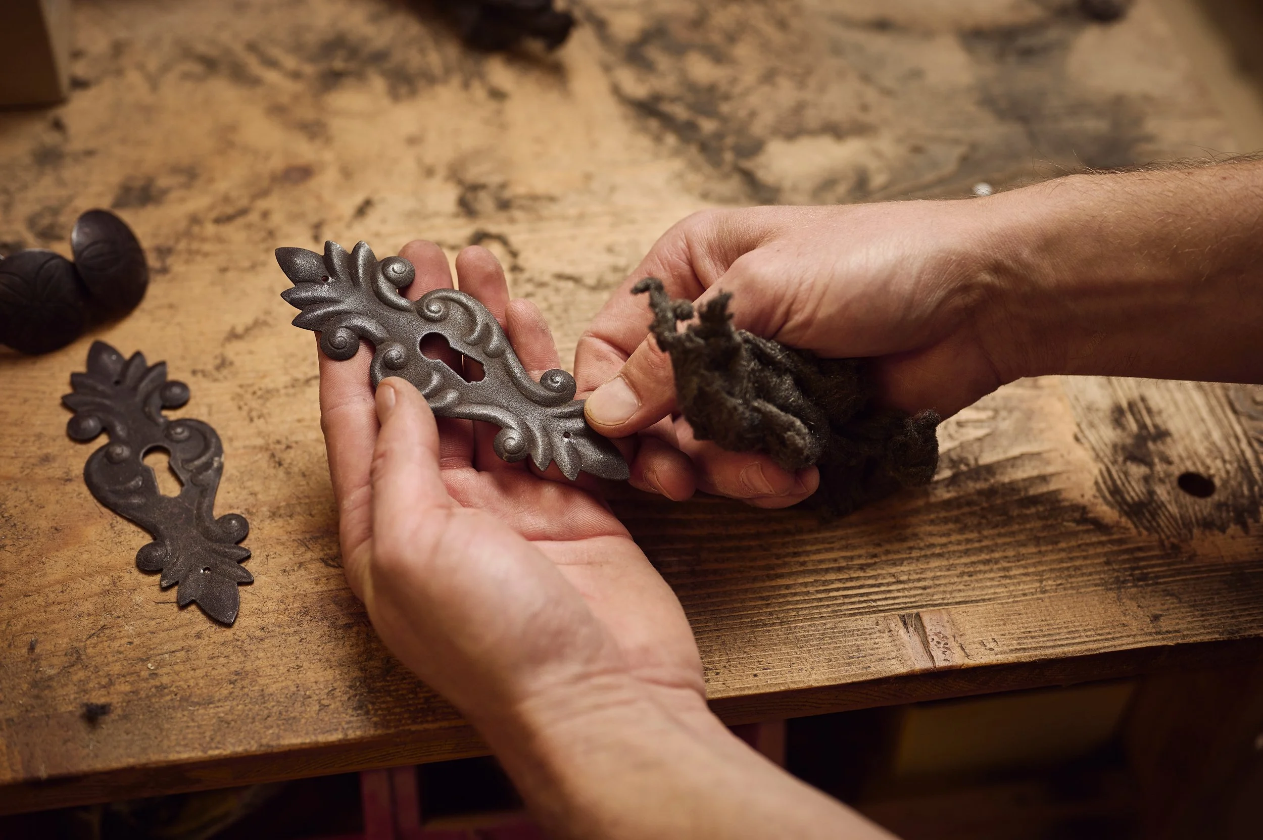 Hand hält ein verzierte Metallplatte, während sie mit einem Tuch arbeitet, auf einem Holztisch.