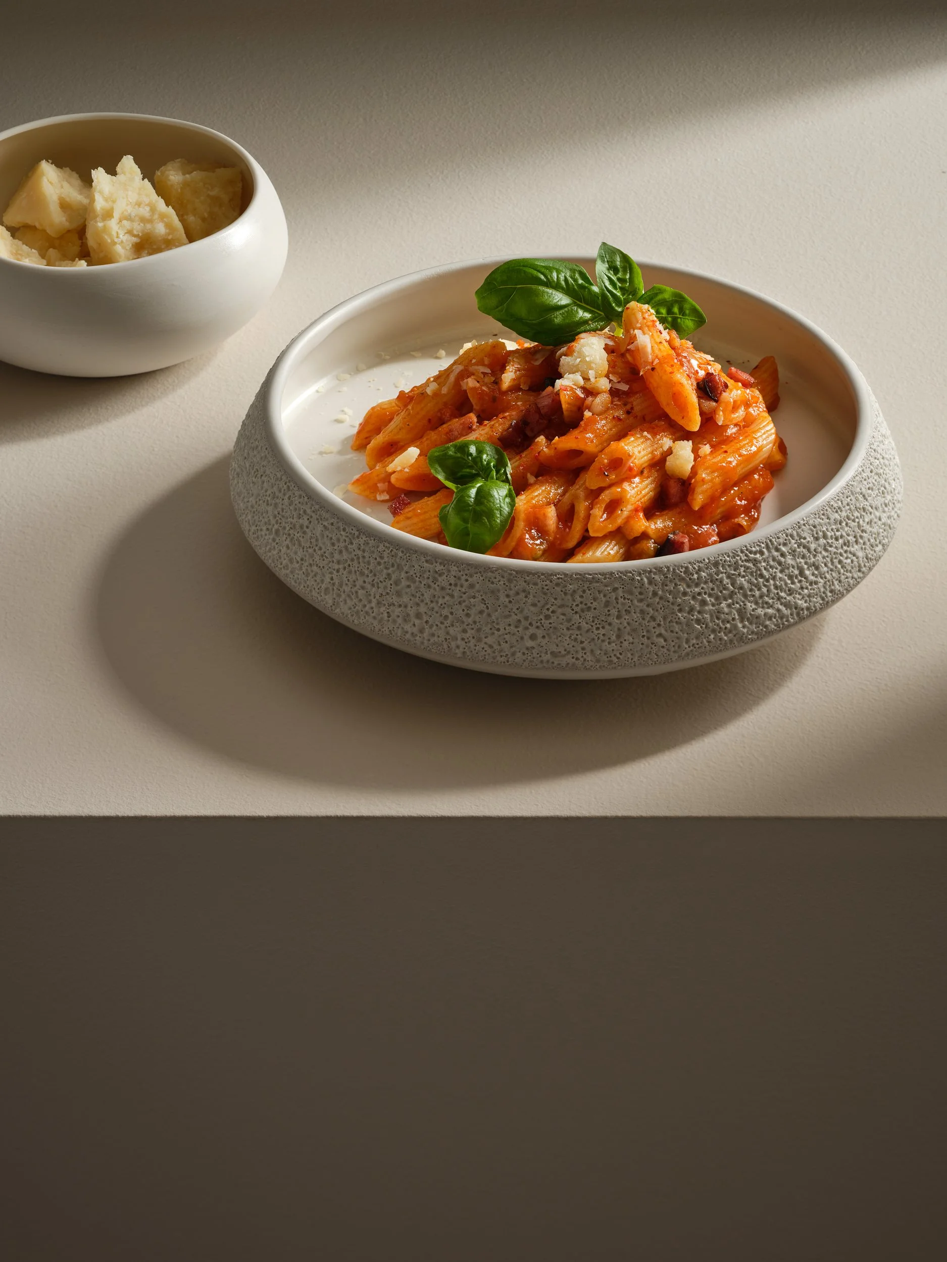 Pasta mit Tomatensauce und frischen Basilikumblättern, dazu eine kleine Schüssel mit Parmesan