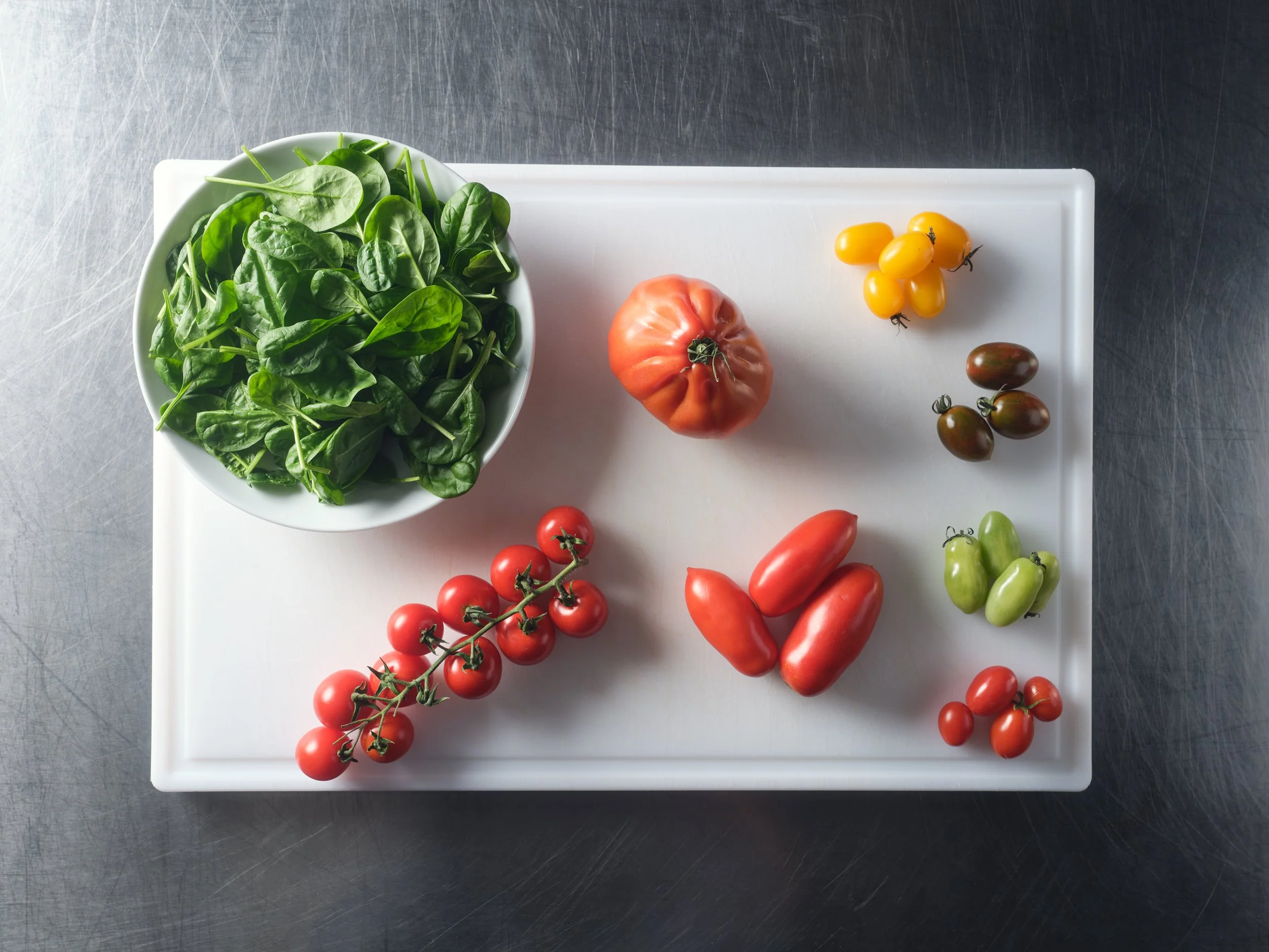 Verschiedene frische Tomaten und Babyspinat auf einem weißen Schneidebrett