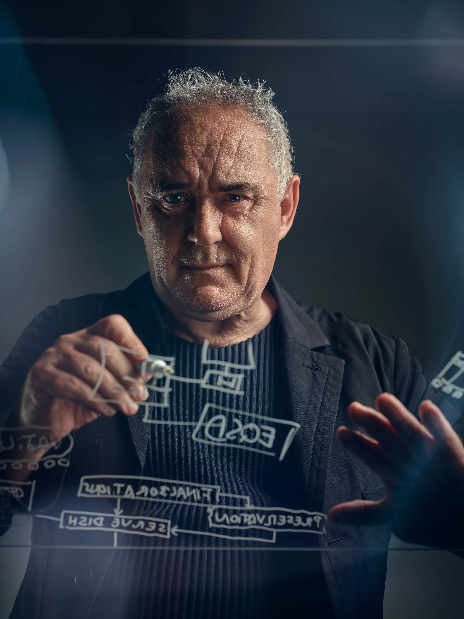 Ein Mann schreibt mit einem Marker auf eine Glasplatte. Auf der Glasplatte sind umgekehrte Begriffe und Diagramme zu erkennen. Der Hintergrund ist dunkel.