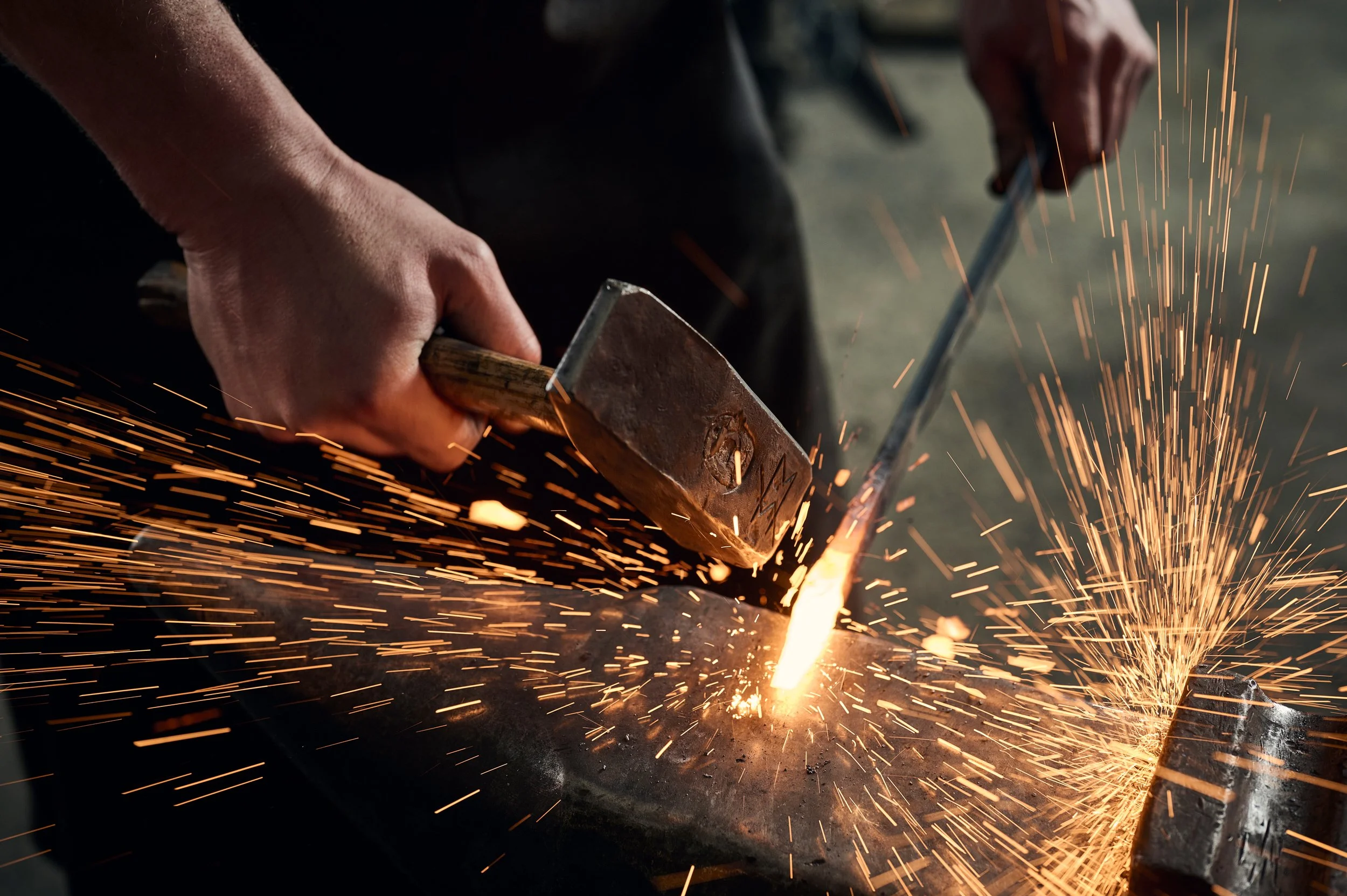 Ein Handwerker schlägt mit einem Hammer auf ein Metallstück, wodurch Funken sprühen.