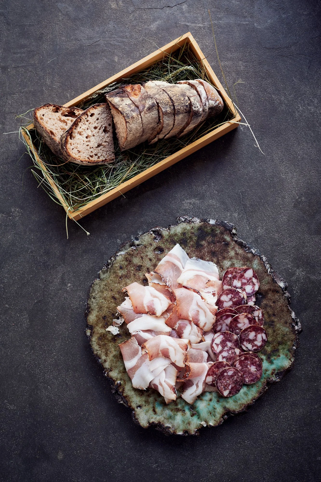 Brett mit verschiedenen Wurstsorten, darunter Schinken und Salami, sowie Käse und Antipasti, auf einer grünen Platte.