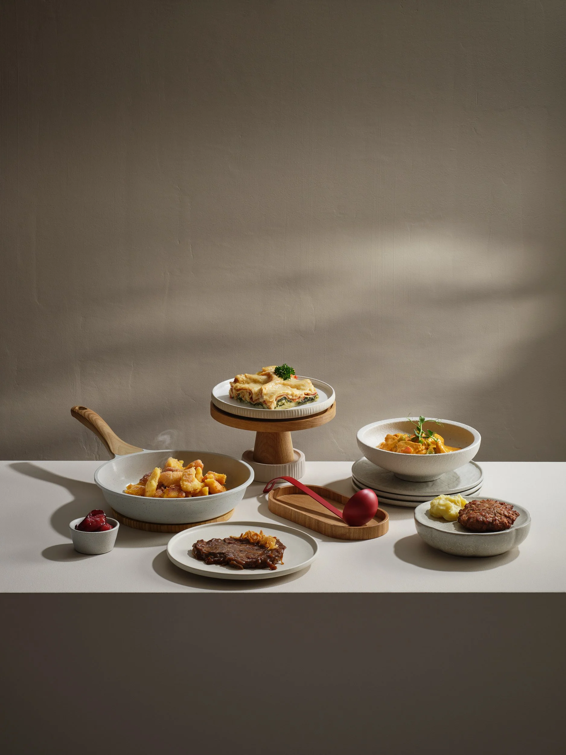 Verschiedene deutsche Gerichte auf weißem Tisch, darunter Rinderroulade, Kartoffeln, Gulasch, Auflauf und Fleischklops, mit Beilagen und Deko.