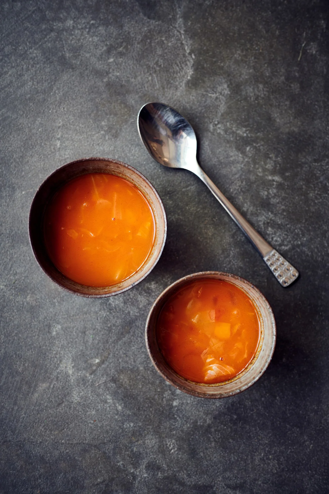 Drei Tassen mit orangefarbener Suppe auf einem dunklen Tisch, daneben ein Silberschopf
