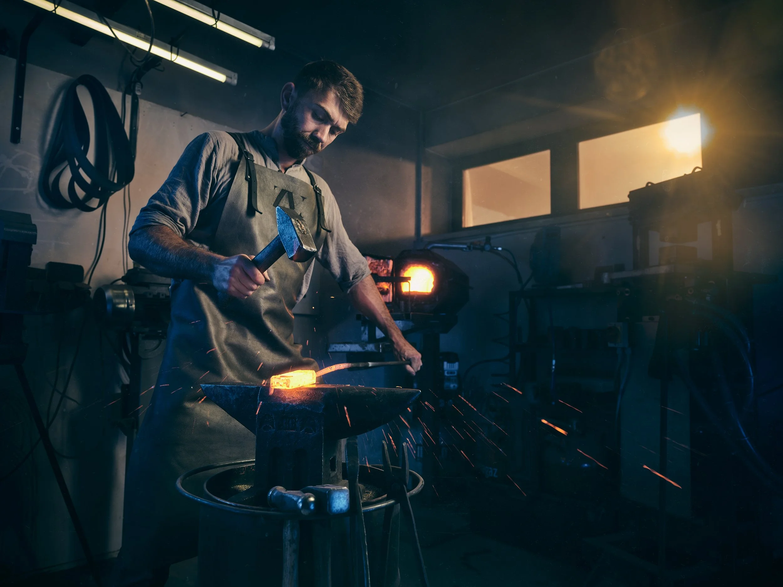 Ein Schmied arbeitet in einer Werkstatt, trägt eine Lederschürze und benutzt einen Hammer, um ein glühendes Metallstück auf einem Amboss zu bearbeiten. Funken fliegen in der Luft, und im Hintergrund ist ein offen gebranntes Feuer zu sehen.