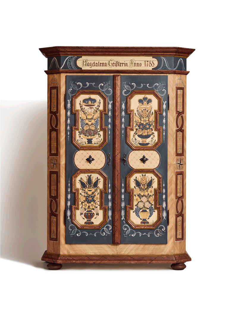 Ein handbemalter Schrank mit dekorativen Blumenmustern auf den Türen, umrahmt von Holzrahmen und -verzierungen, mit einer Inschrift auf dem oberen Rand.