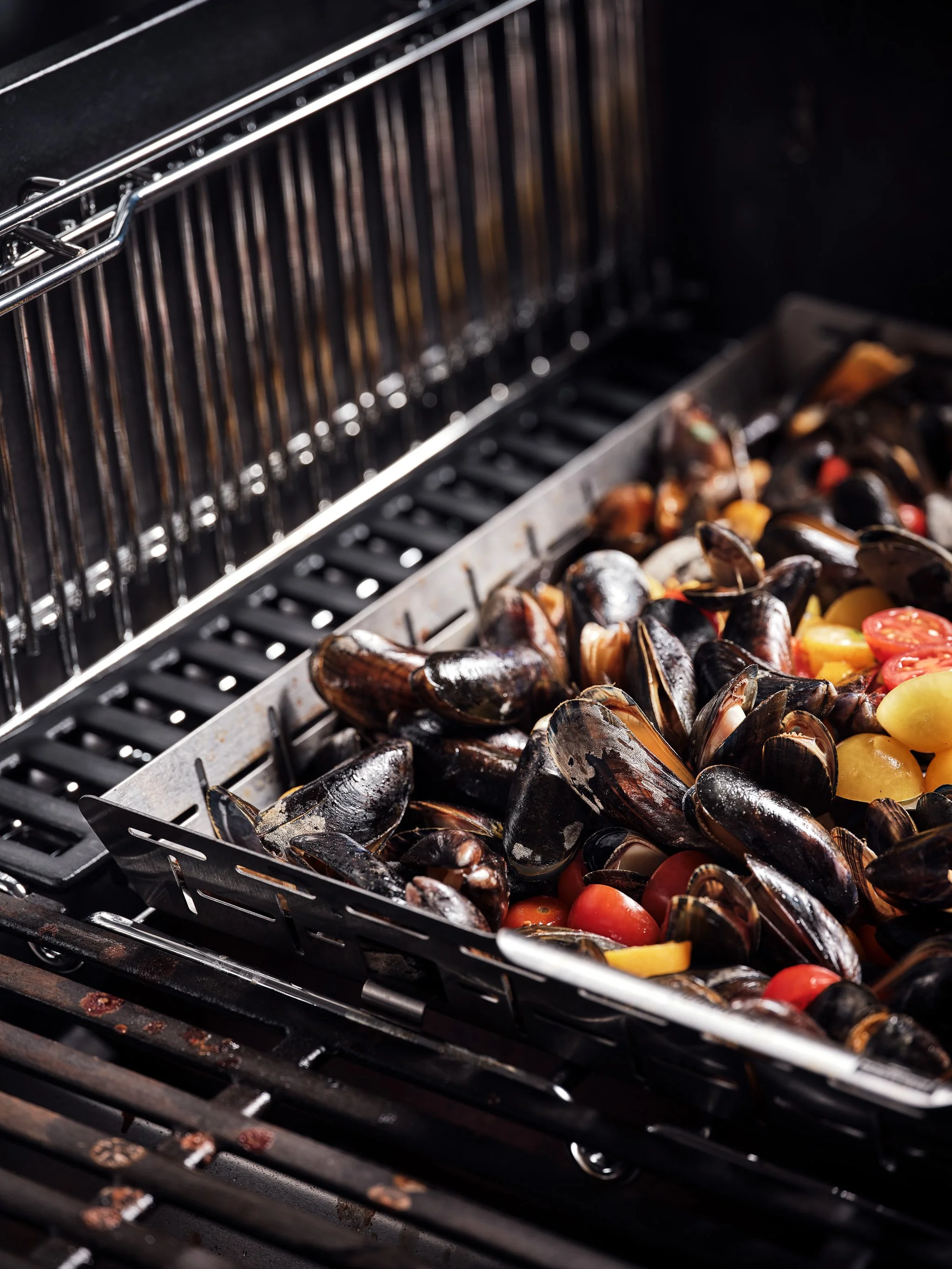 Miesmuscheln und Gemüse in einer Grillpfanne auf einem Grillrost.