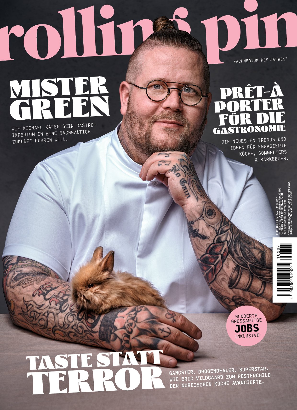 Pinkaki-Magazin-Cover mit Michael Green, der einen tätowierten Arm hat, eine Katze auf seinem Arm, trägt Weiß, trägt runde Brille, hat einen Mannbun, und es ist Text auf Deutsch mit Titeln wie 'Mister Green' und 'Taste statt Terror'.