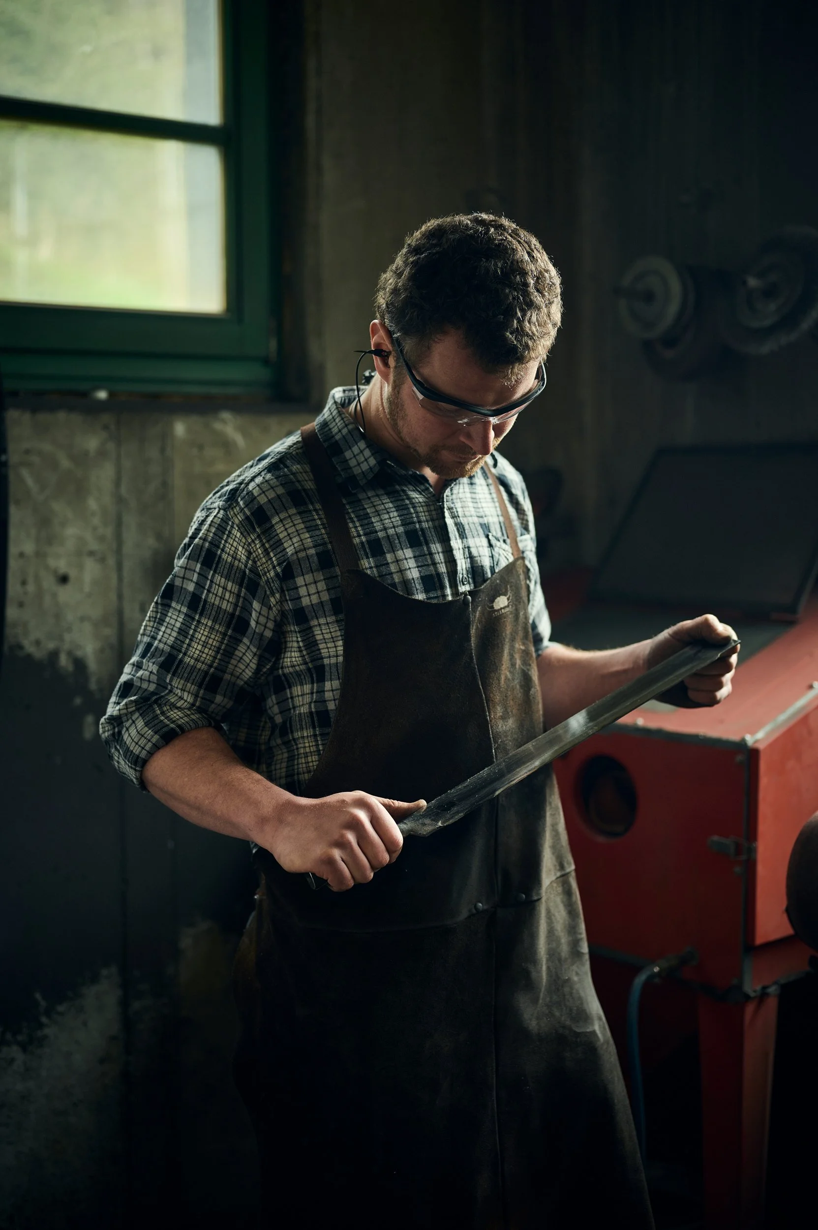 Mann in Werkstatt mit Schutzbrille, hält Metallsäge und arbeitet an Metallstück.
