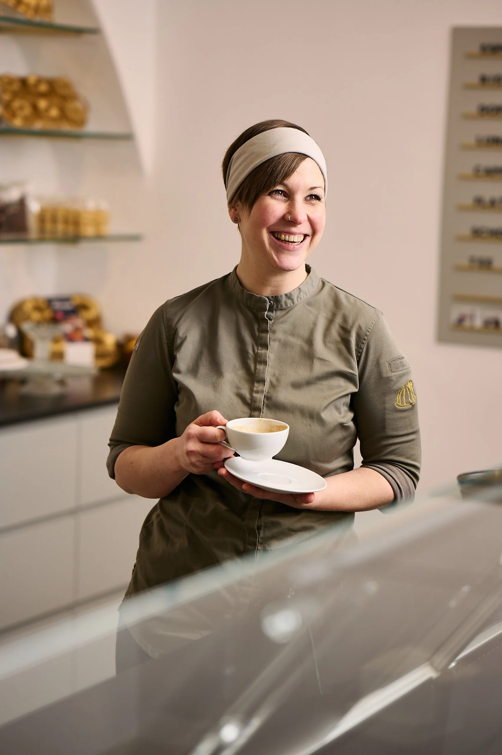 Frau mit Kurzhaarfriseur und weißem Stirnband hält eine Tasse Kaffee und lächelt in einer modernen Küche.