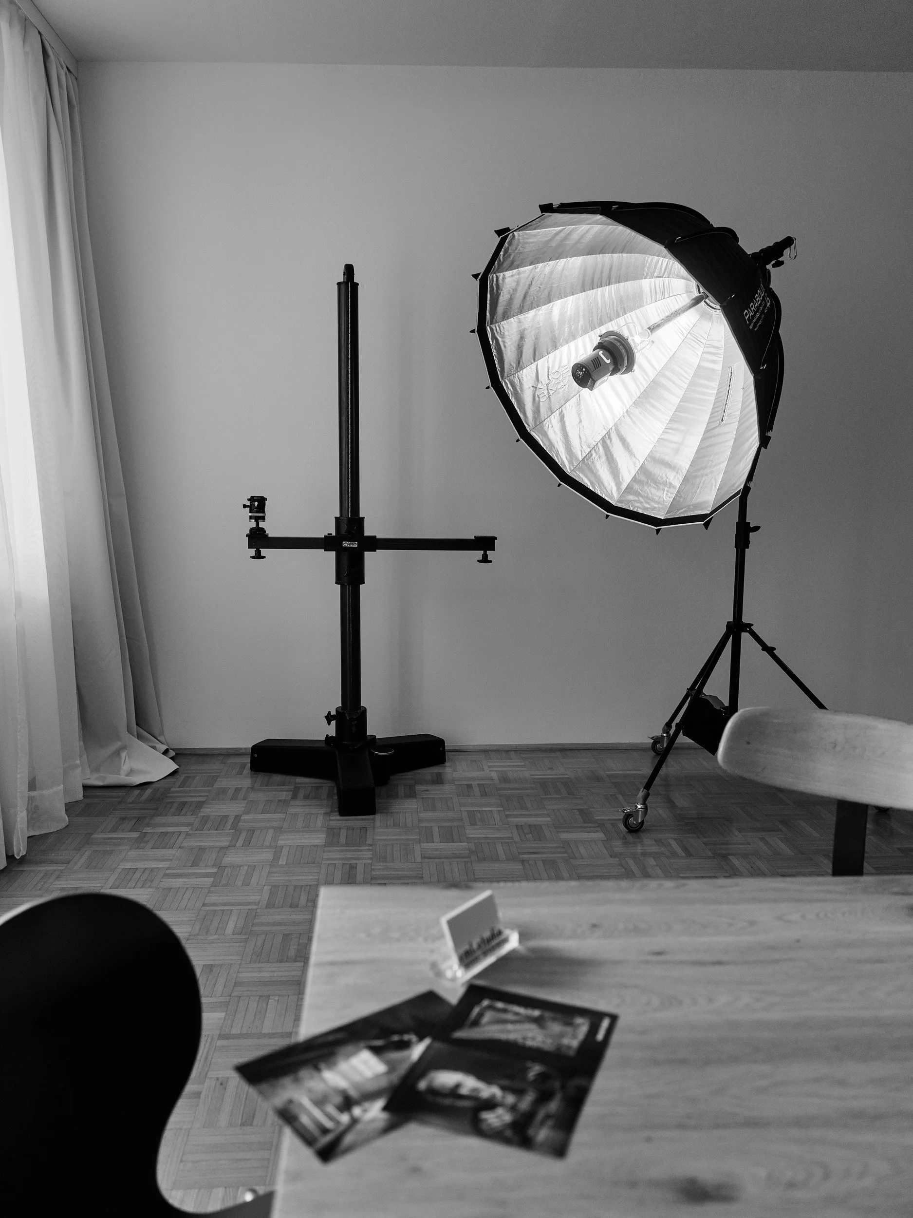 Fotostudio mit Kamera, Studioblitzlicht, Lichtsocke und Stativ in einem Raum mit Holzboden und weißen Wänden.