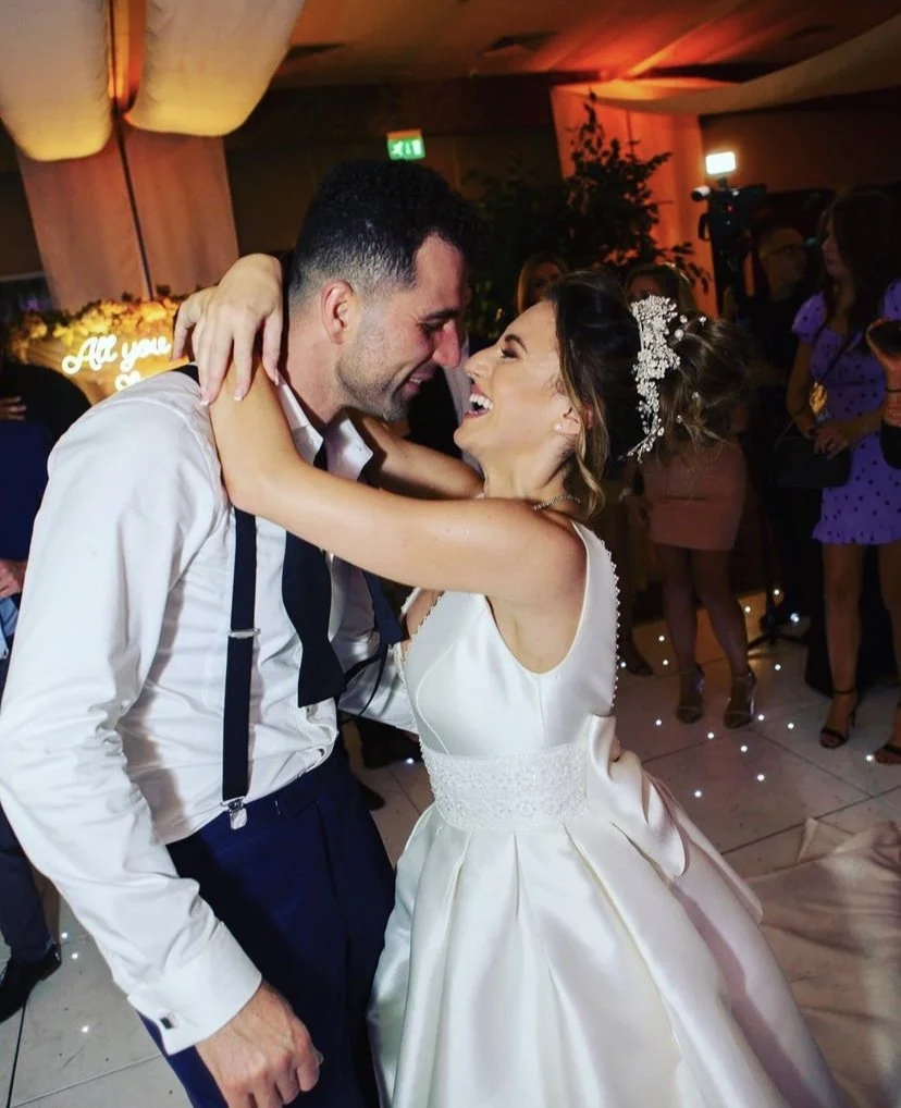 A bride and groom sharing a joyful dance at their wedding reception with friends in the background.