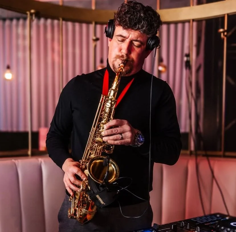 A man listening to music with headphones while playing a golden saxophone in a stylish indoor setting.