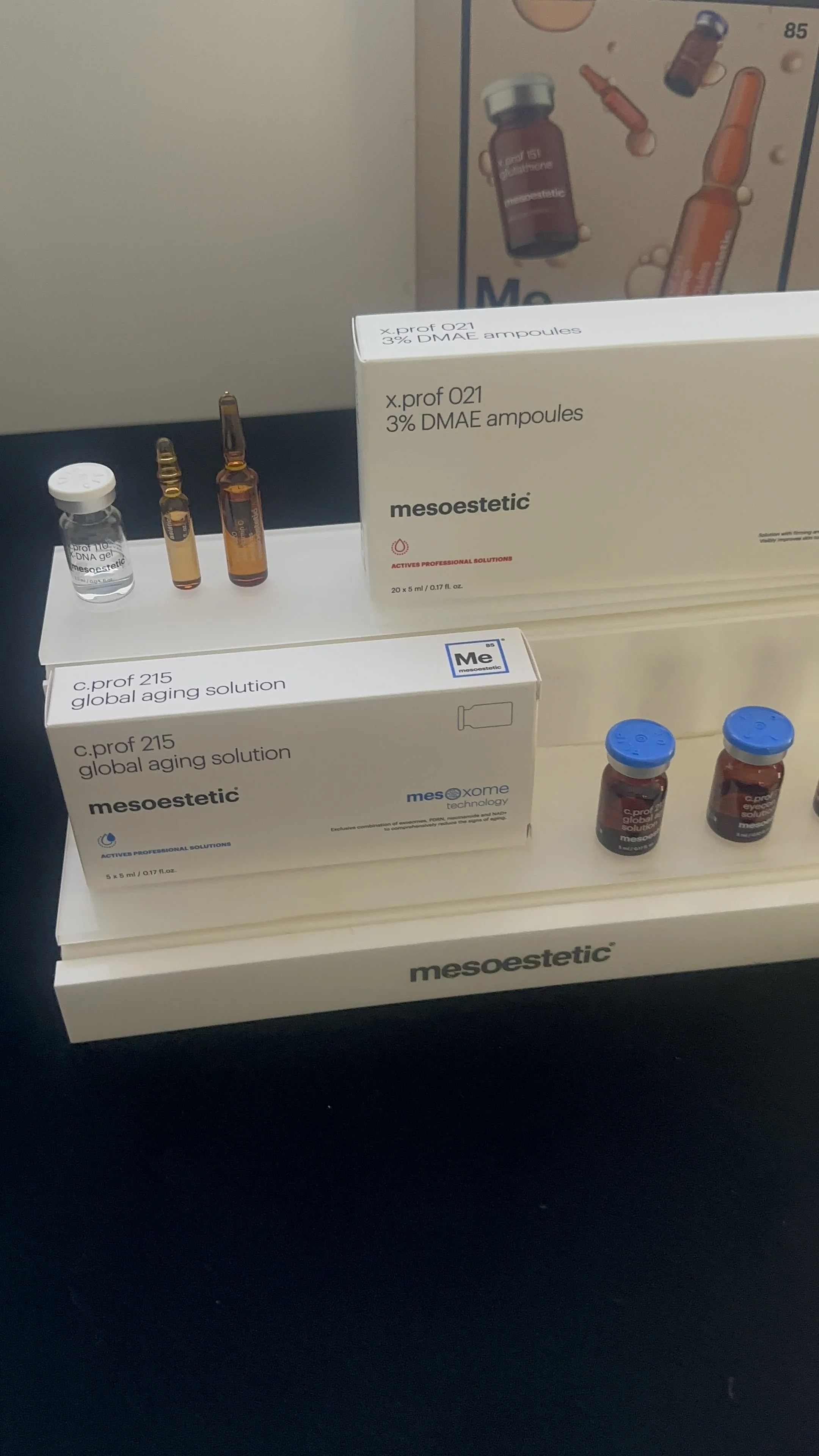 A display of medical vials and boxes labeled mesoestetic, including ampoules for skincare treatments such as 3% DMAE ampules and global aging solution.