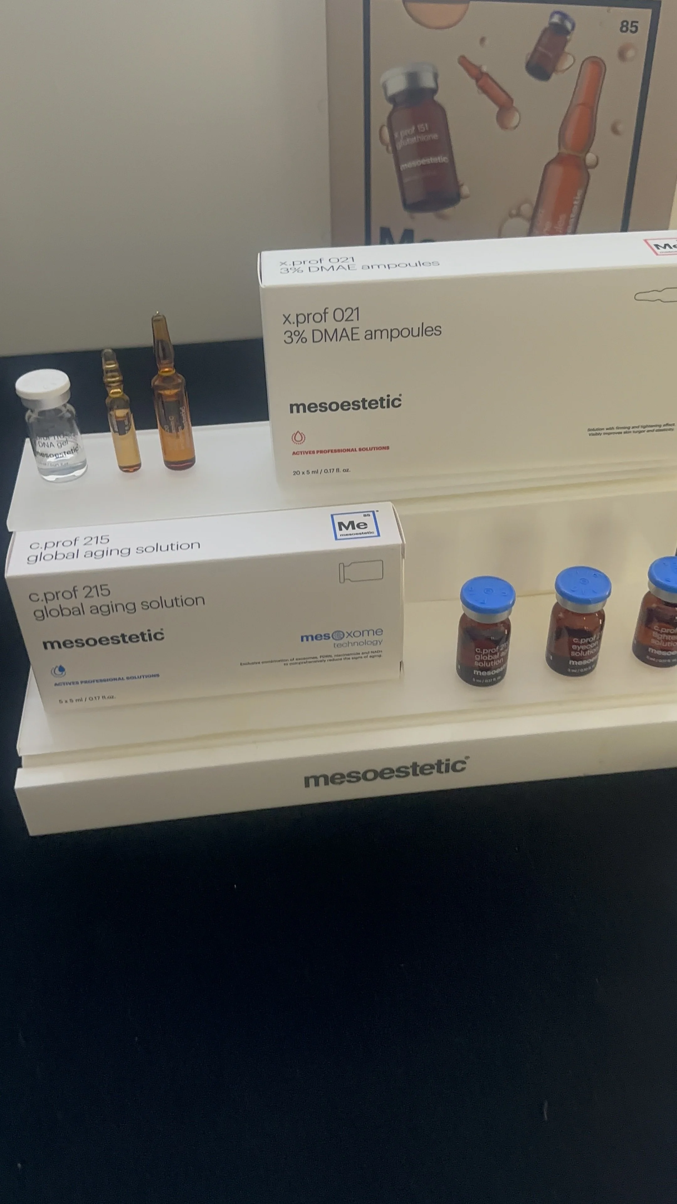 Display of medical products, including small vials and boxes of mesoestetic skincare solutions on a black surface.